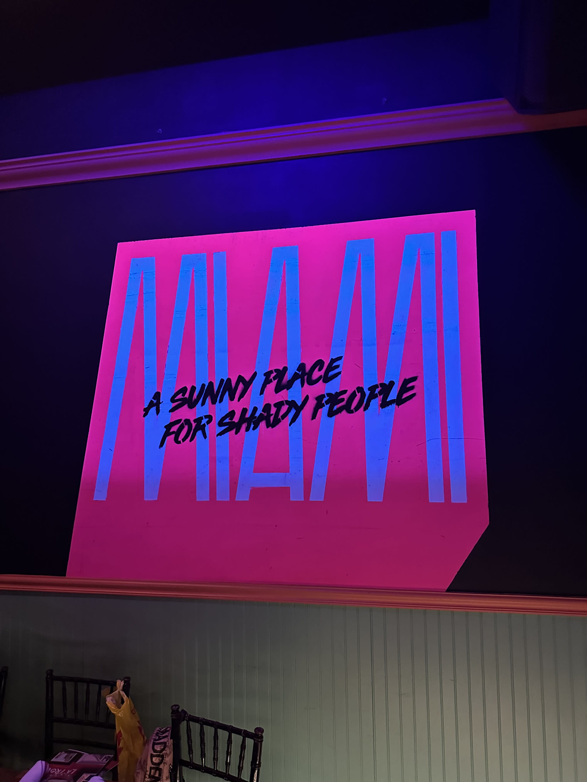 The image shows a neon sign with the text “A SUNNY PLACE FOR SHADY PEOPLE” in pink against a dark background.