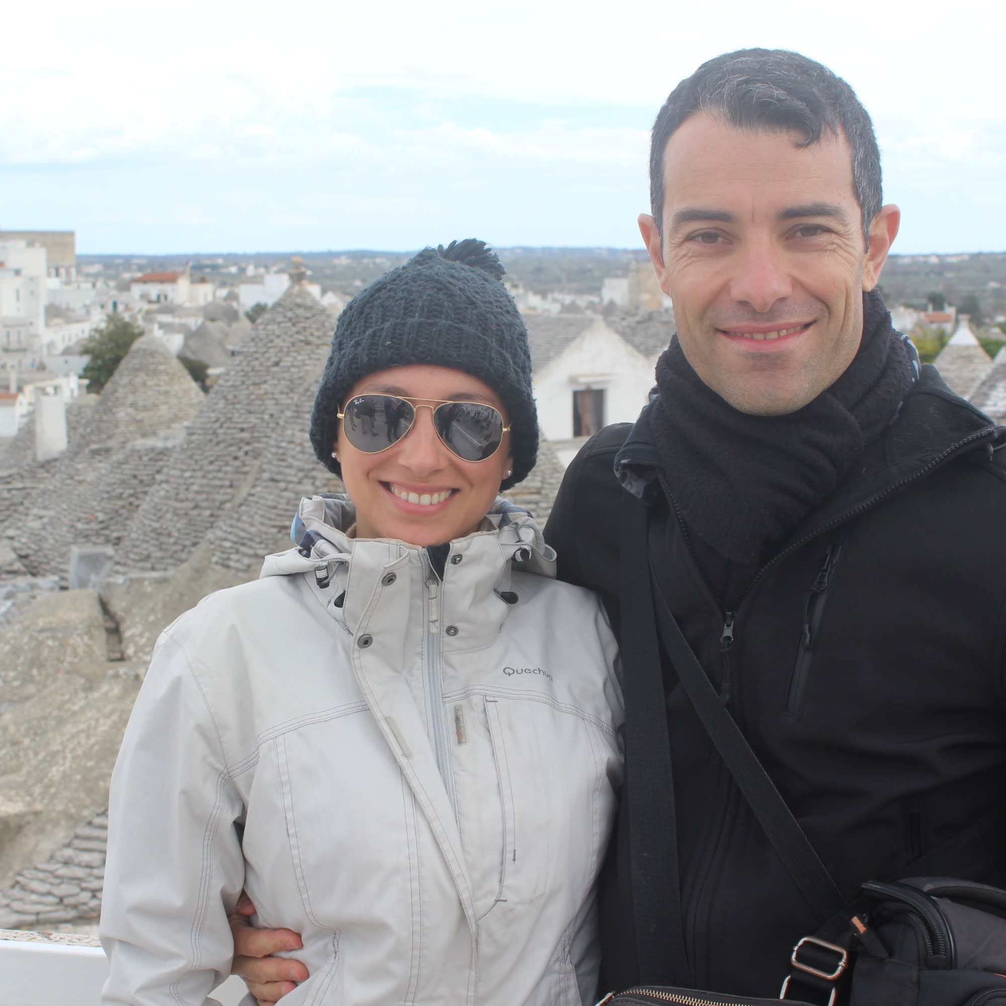 In this picturesque view, two individuals stand before a backdrop of white buildings adorned with conical roofs.