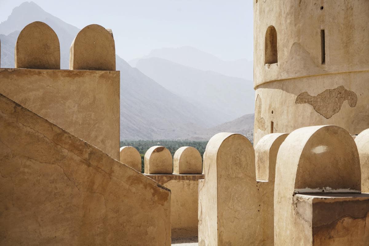 A stone exterior with various arches and mountains in the background.