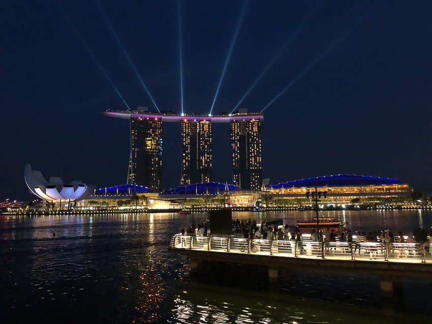 A city on the water at night with light beams shining in the sky