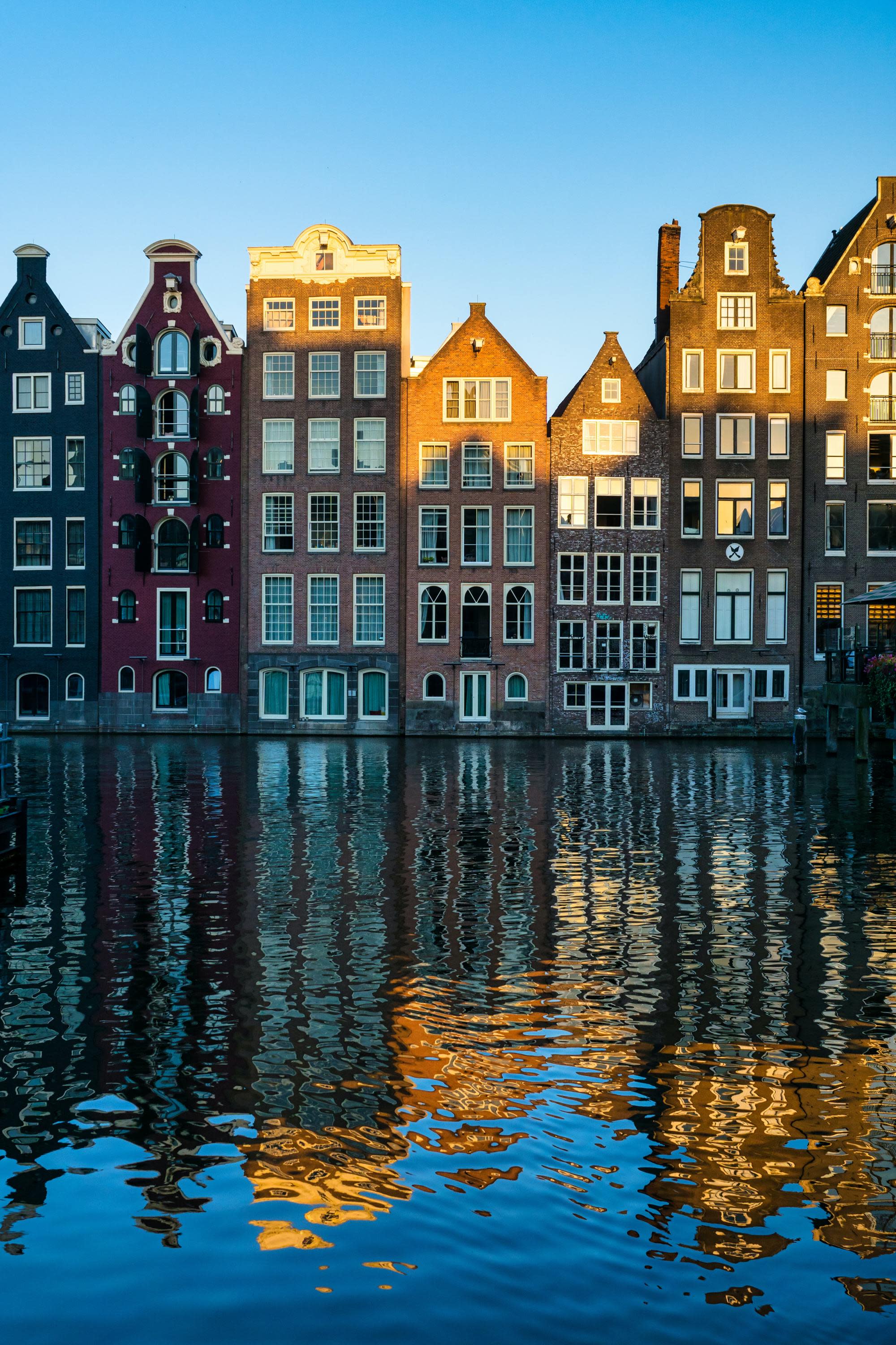 multiple story houses with big white windows on a canal reflect into the water below on a clear day