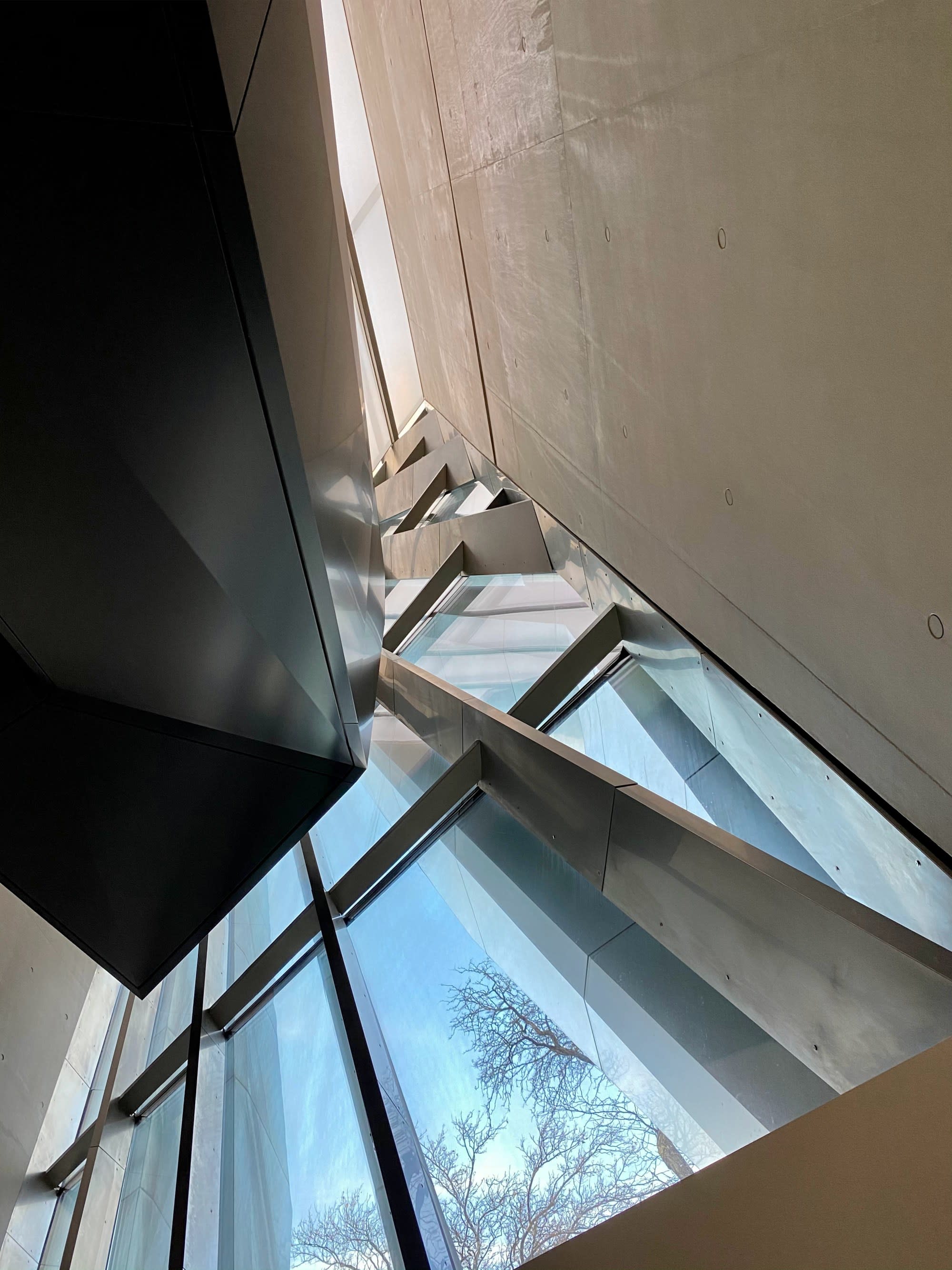 A bottom up view of a white wall and abstract window frame with silver and black beams built in angled directions.