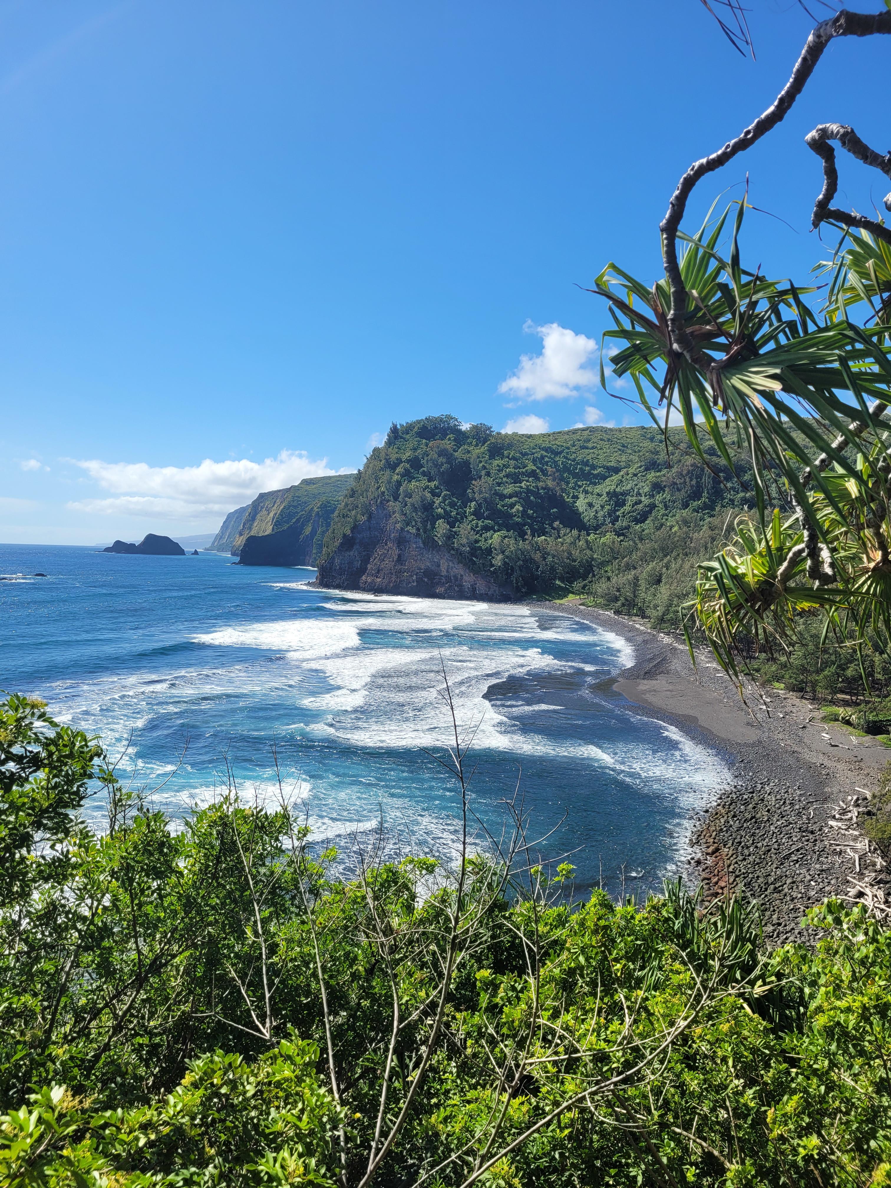 Beach and body of water next to green mountains with blue skies during daytime
