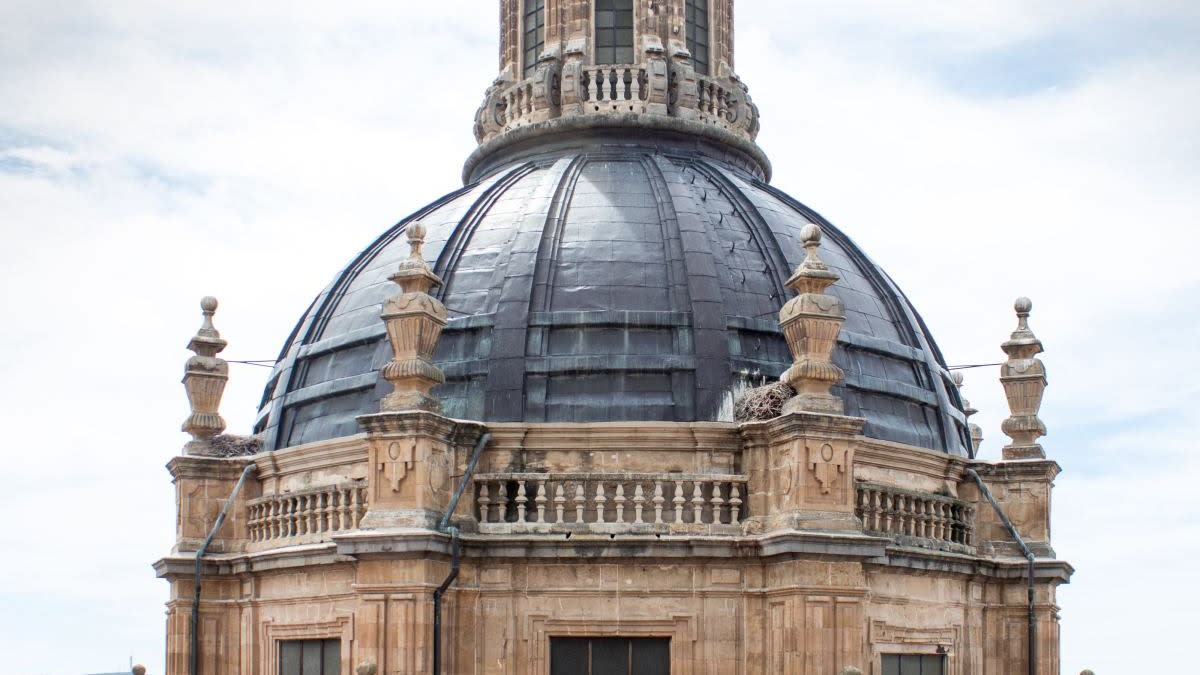 A beautiful old stone building with a dome roof and a spiral at the top with a cloudy blue sky in the background.