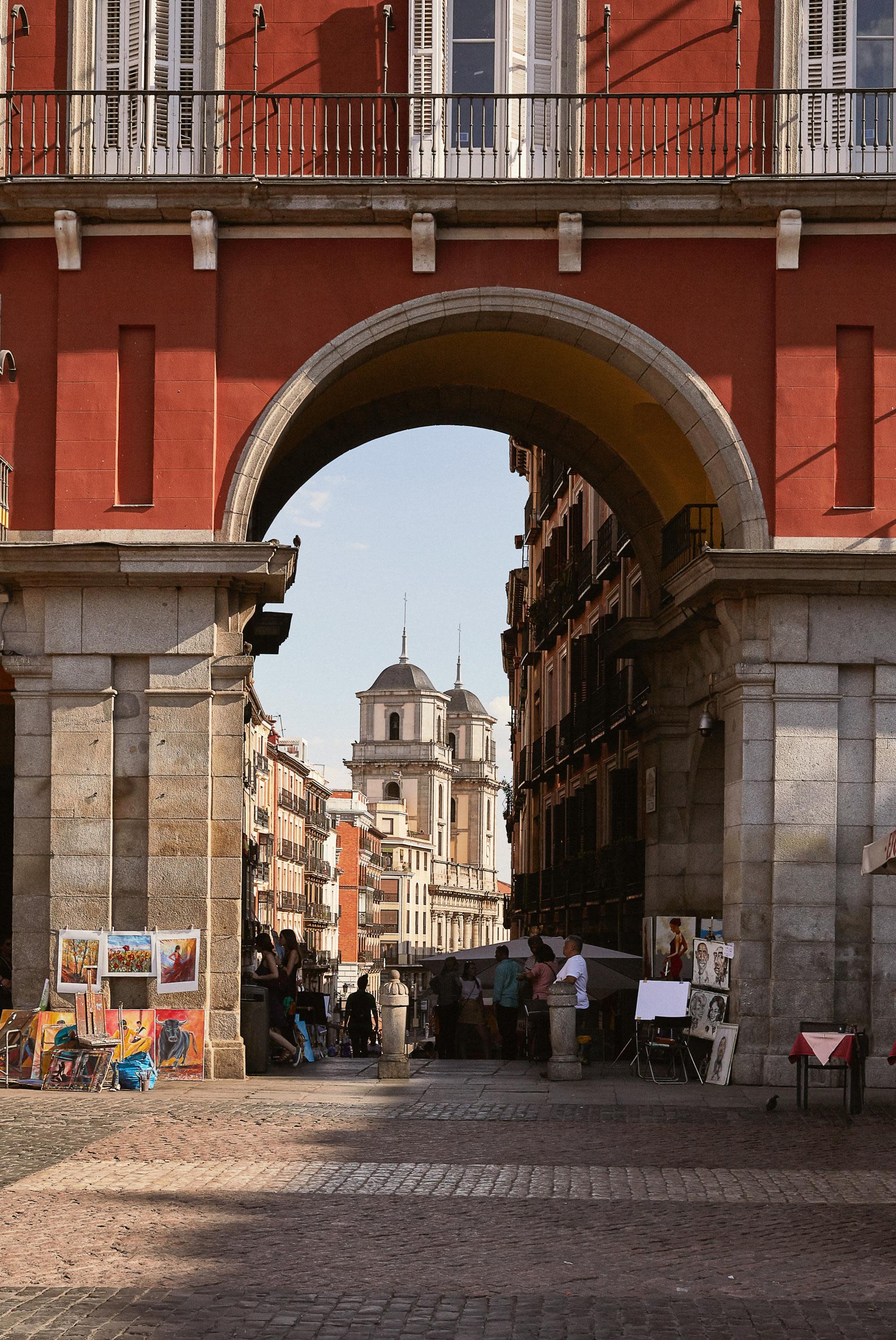 a large archway leads into a narrow city street with vendors and artists