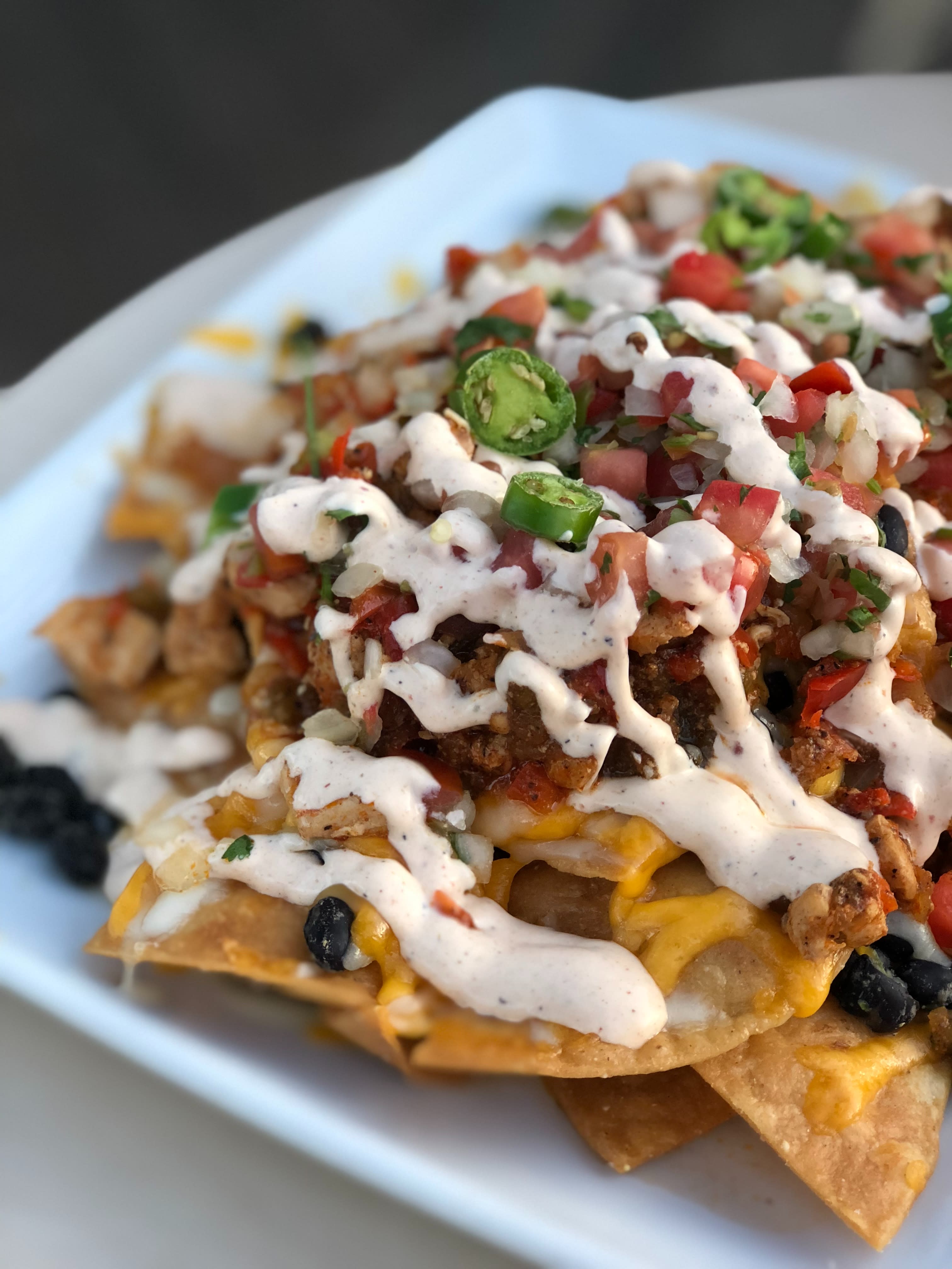 A bowl of nachos with cheese, meat and vegetables.