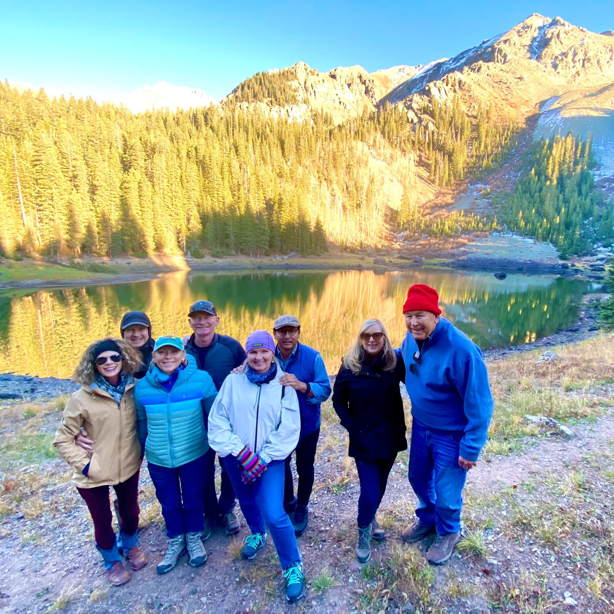 A group of people standing in front of lake among hills.