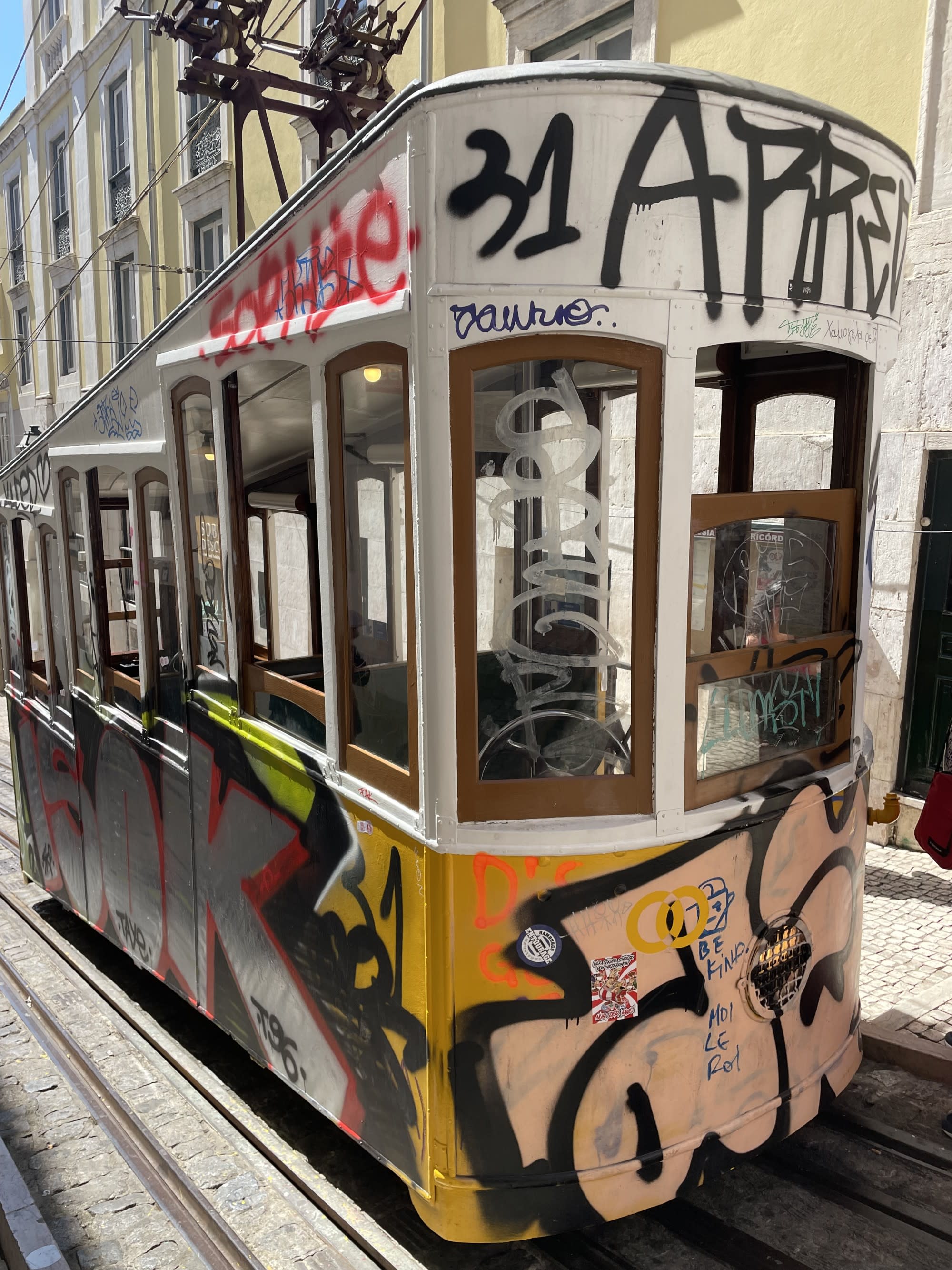 A picture of a multi-colored tram on the road during the daytime covered in street art.