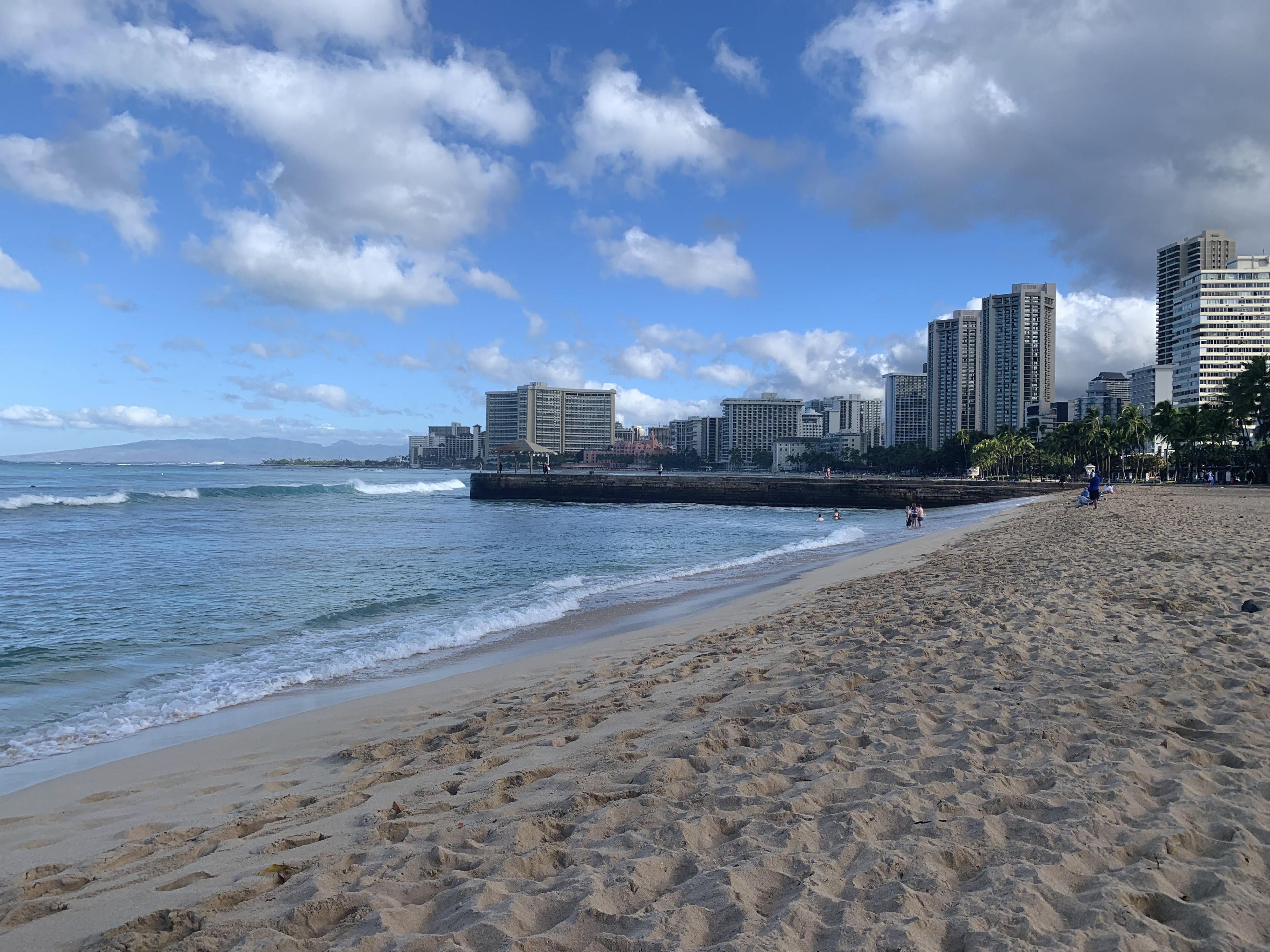 A view of a sandy beach with a city skyline along the coast in the background.