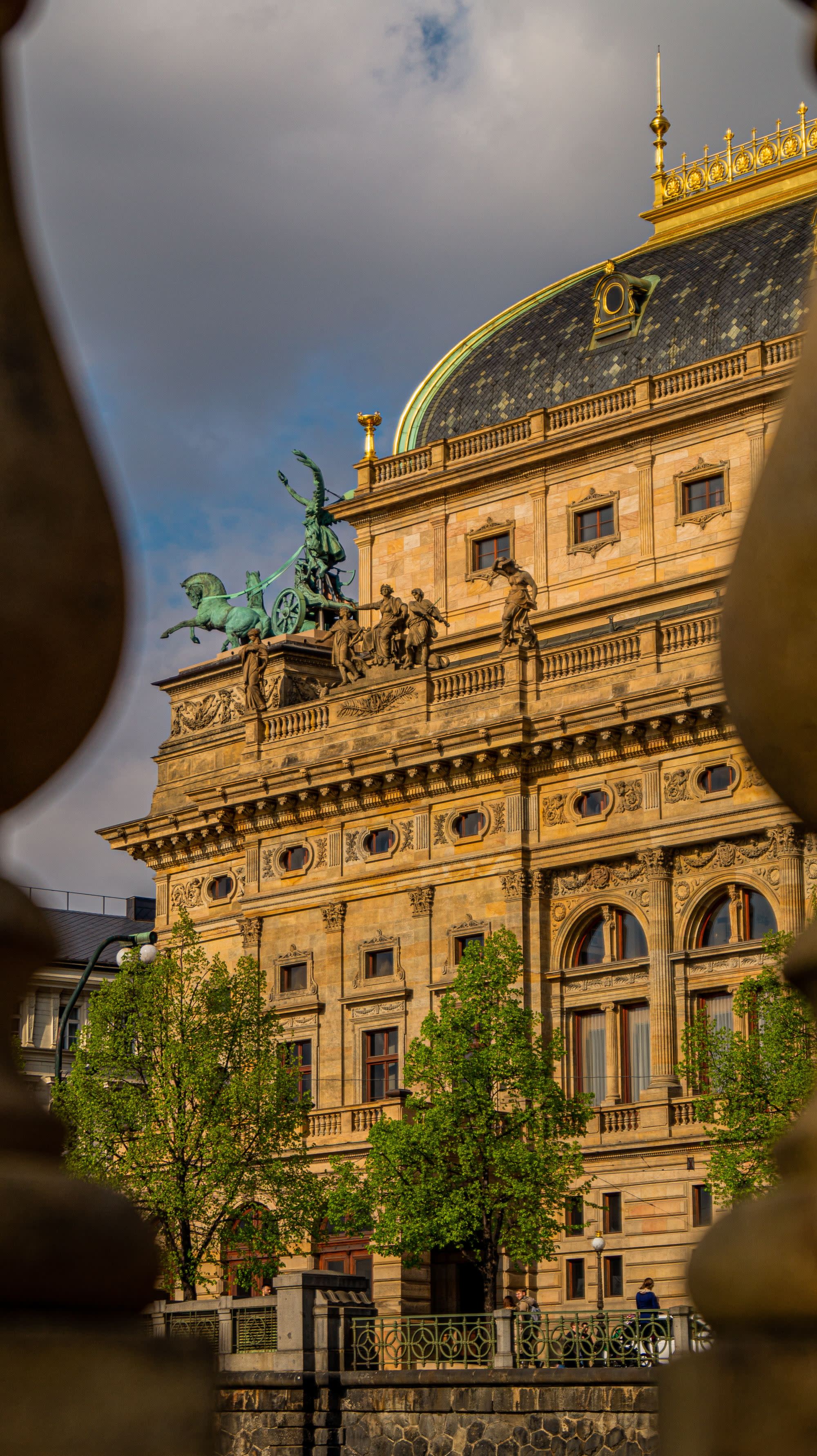 a historic and grand building with trees lining the front on a cloudy day