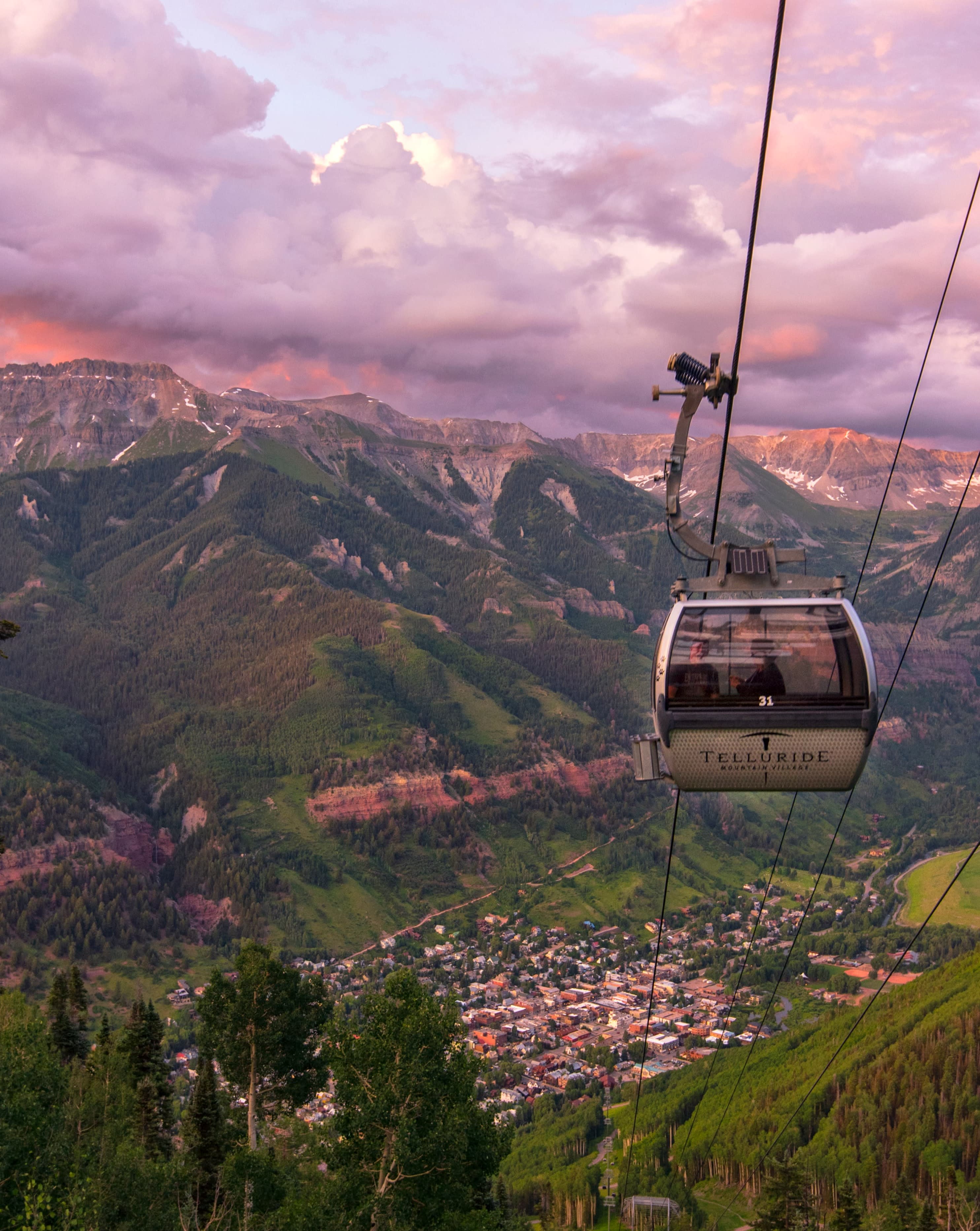 gondola going down a mountain with pink and purple skies, a great thing to do in the summer in Colorado