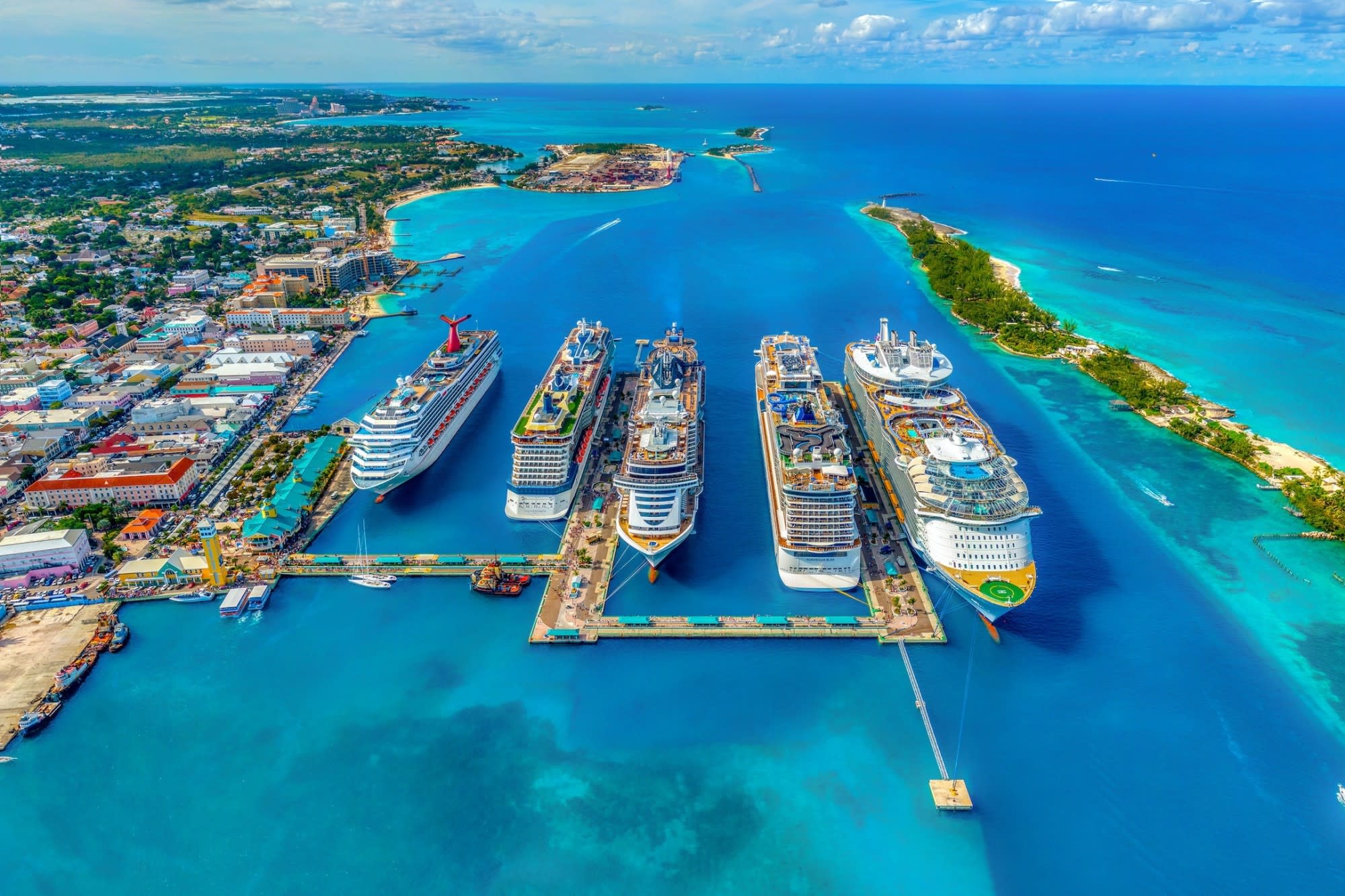 Five cruise ships, including a liner belonging to the Virgin Voyages fleet, are docked at a port in the Bahamas on a sunny day with sapphire blue waters contrasting with the rainbow of colors displayed in the port (photo by Fernando Jorge)