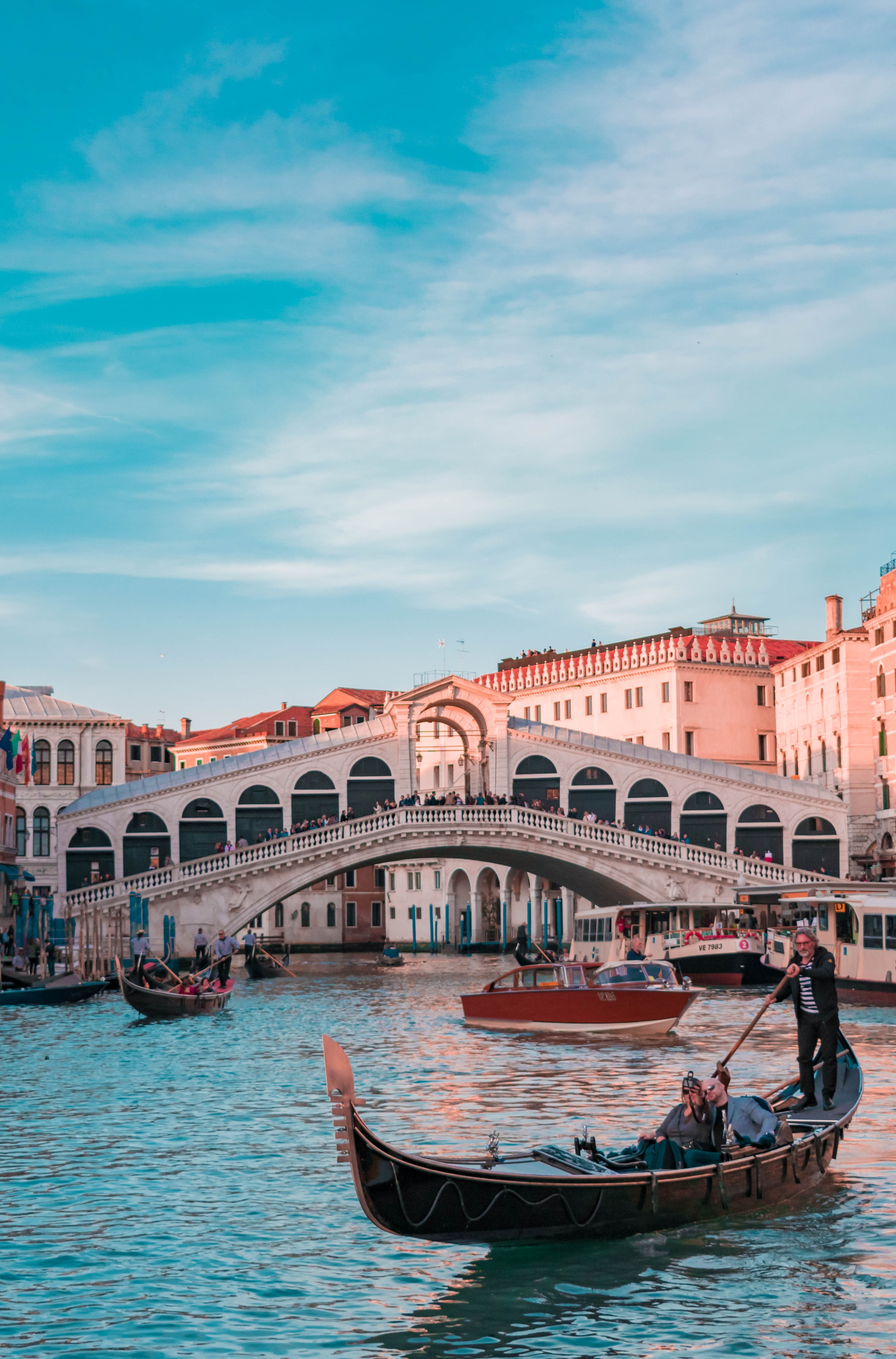 An aesthetic view of a riven passing through the city with a boat in it near the bridge, in Italy.