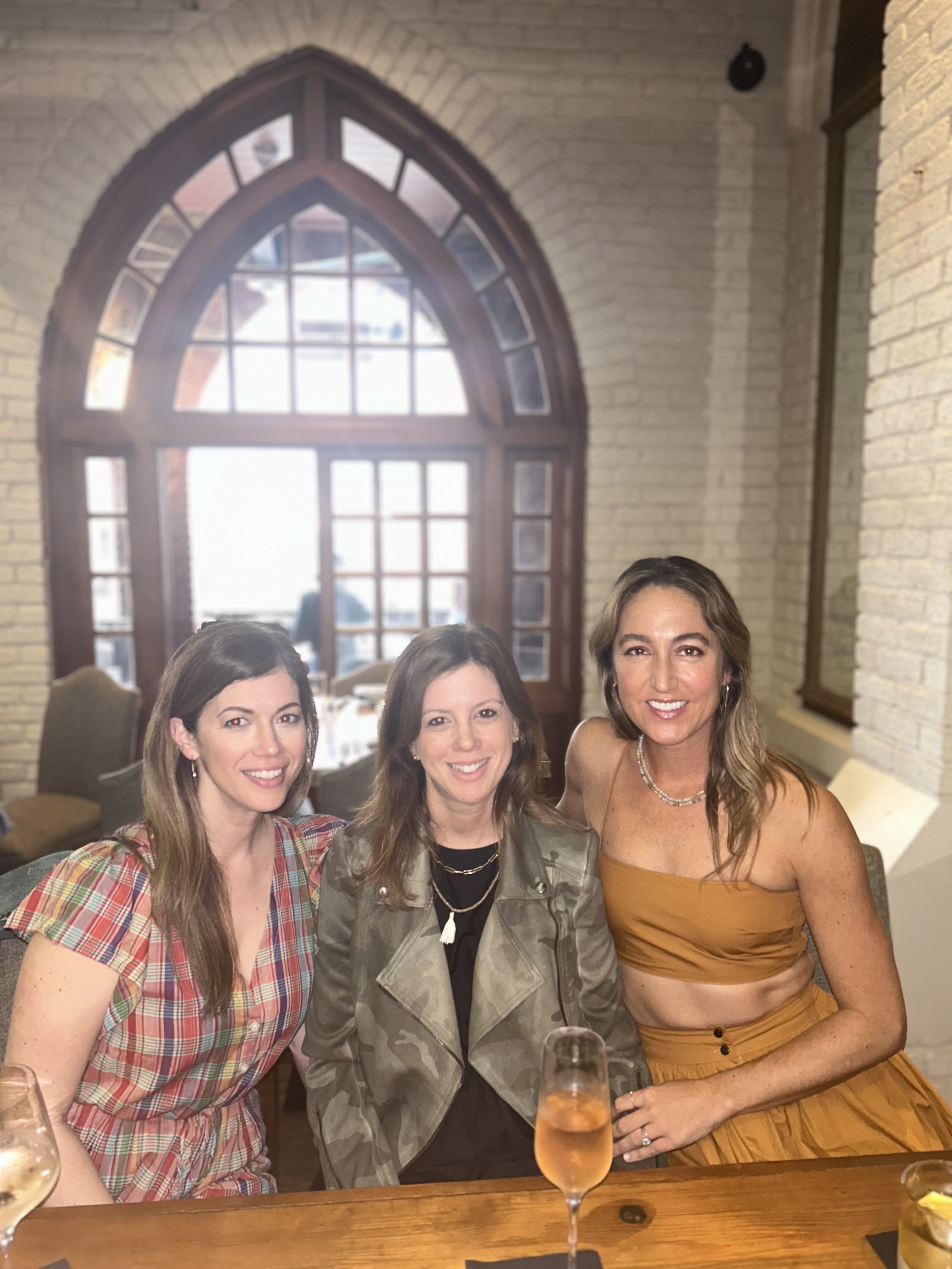 Three girls posing for a photo in front of a window.