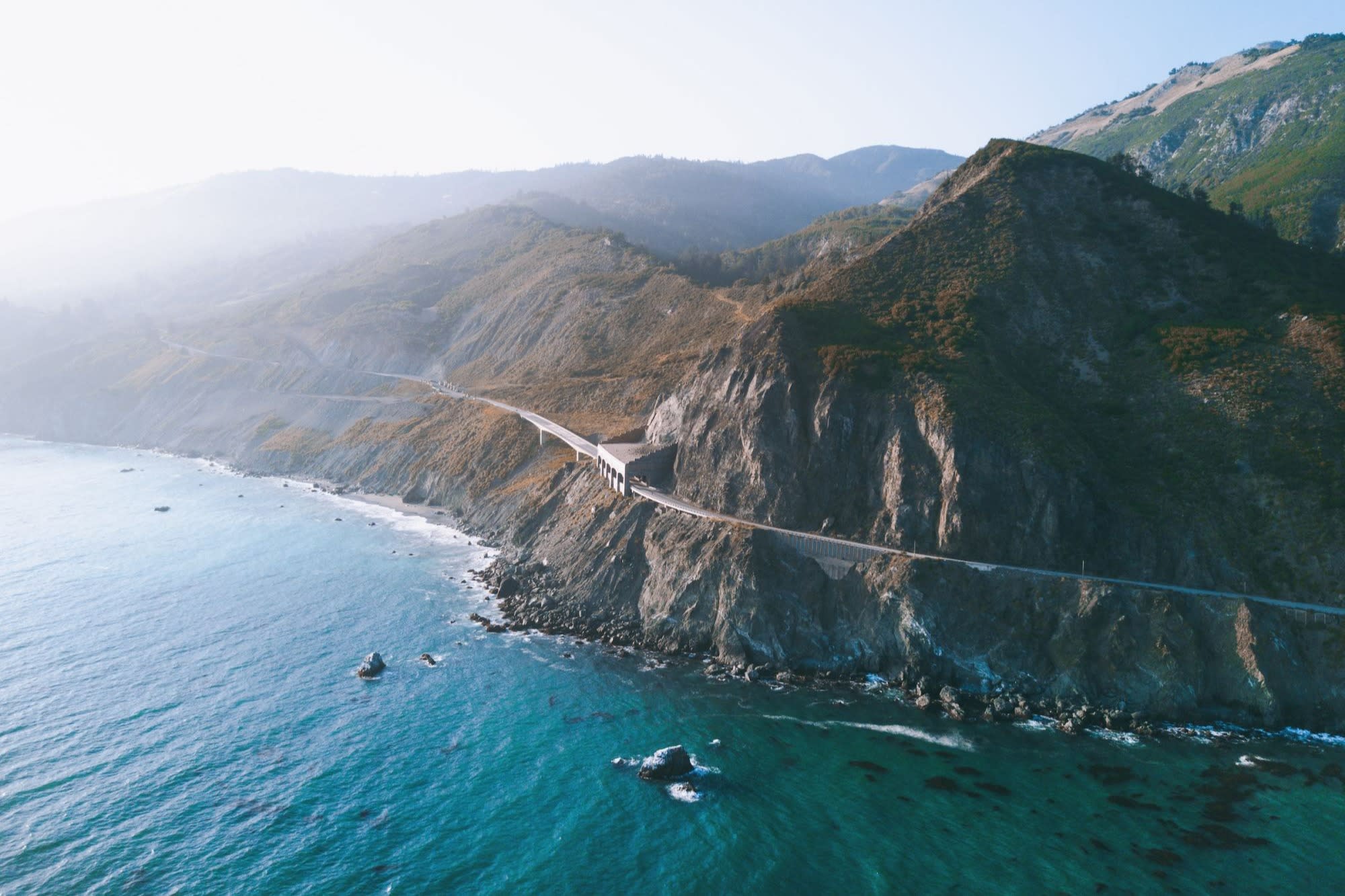 The scenic coast of Big Sur, with the Pacific Coast Highway running along the cliffs beneath fog-covered hills (photo by Thomas Ciscewski)