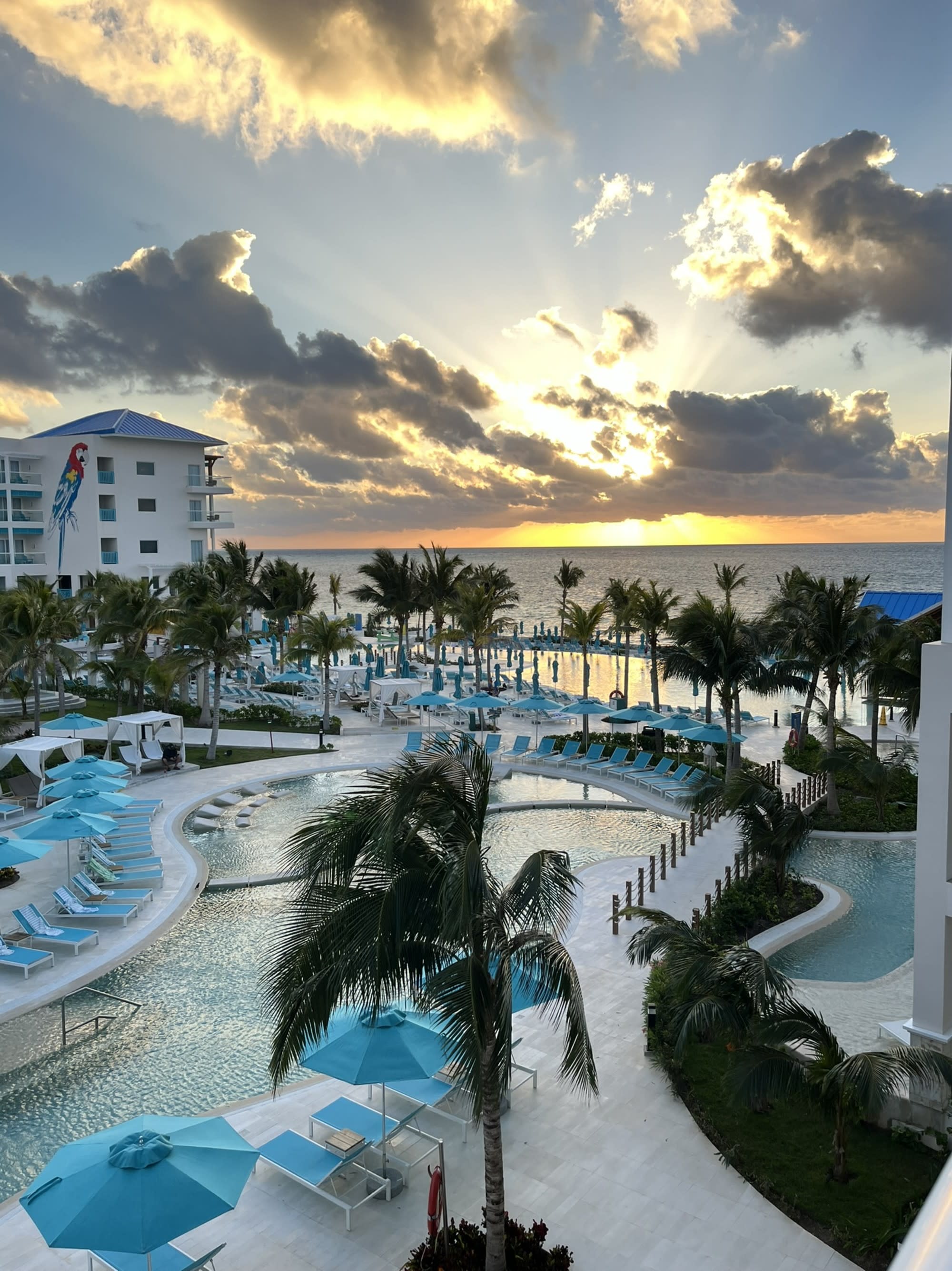 The image shows a sunset view over a resort with a pool and palm trees at sunset.