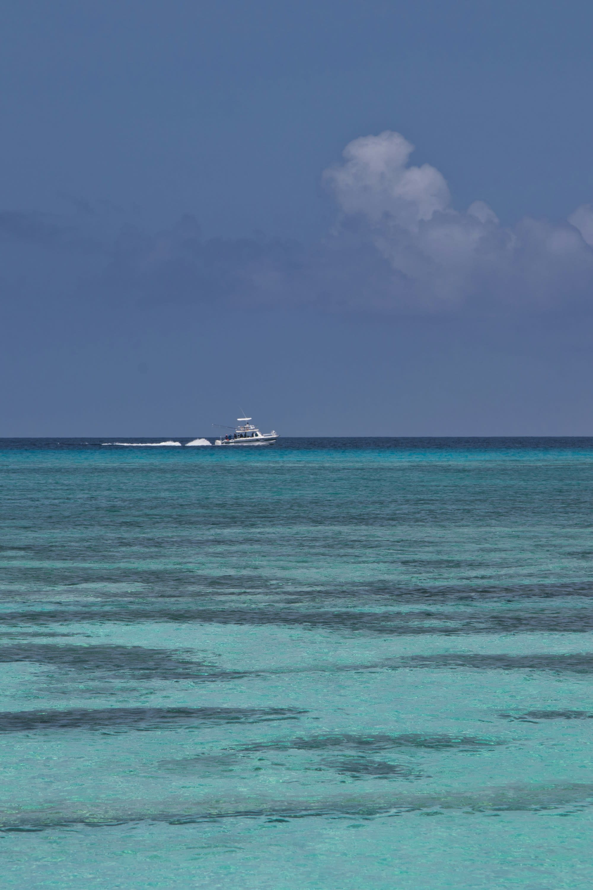 Different shades of turquoise ocean with blue sky and a boat in the far distance.