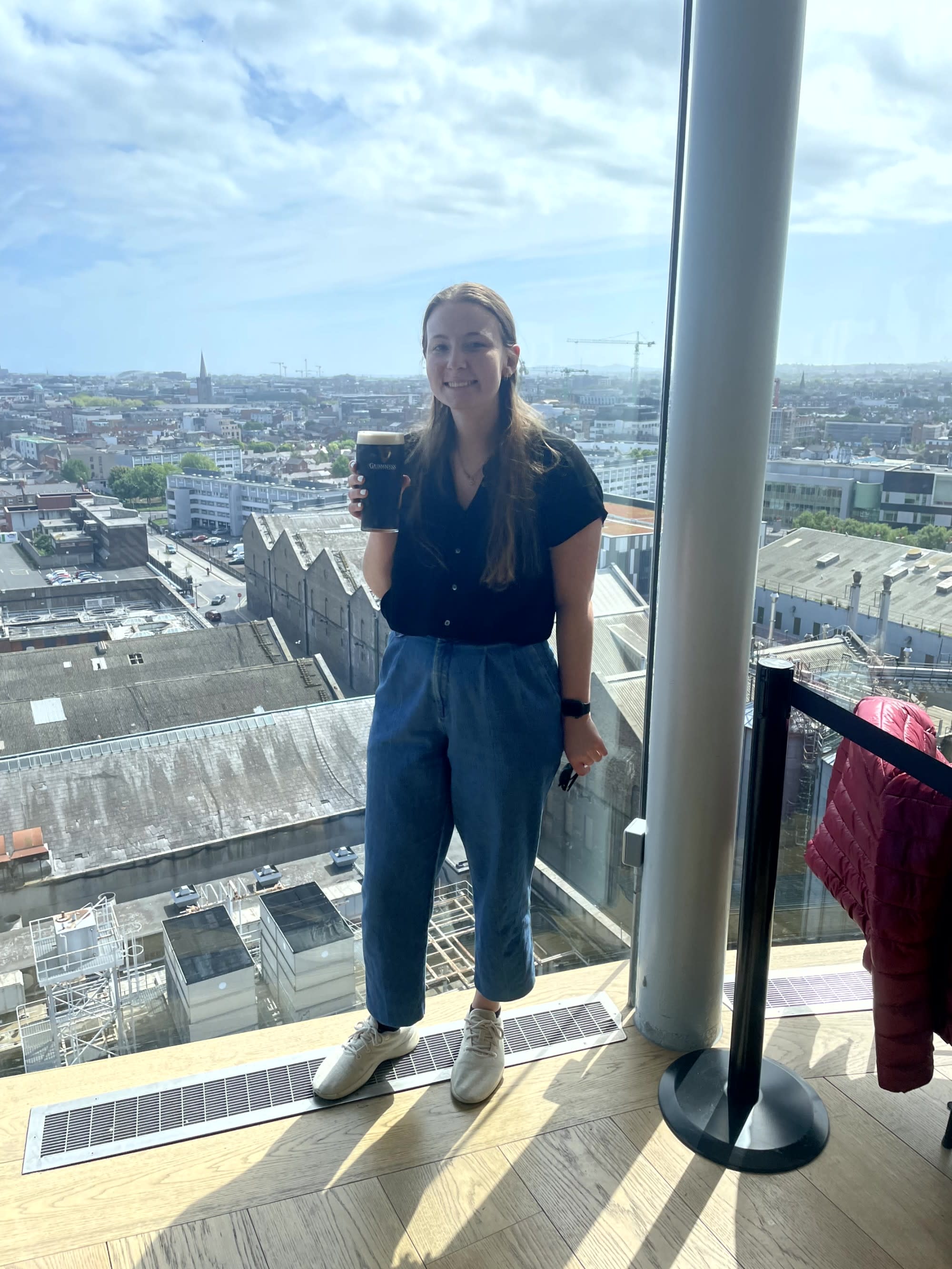 A girl posing at the Guinness Storehouse Roof holding a glass of drink.