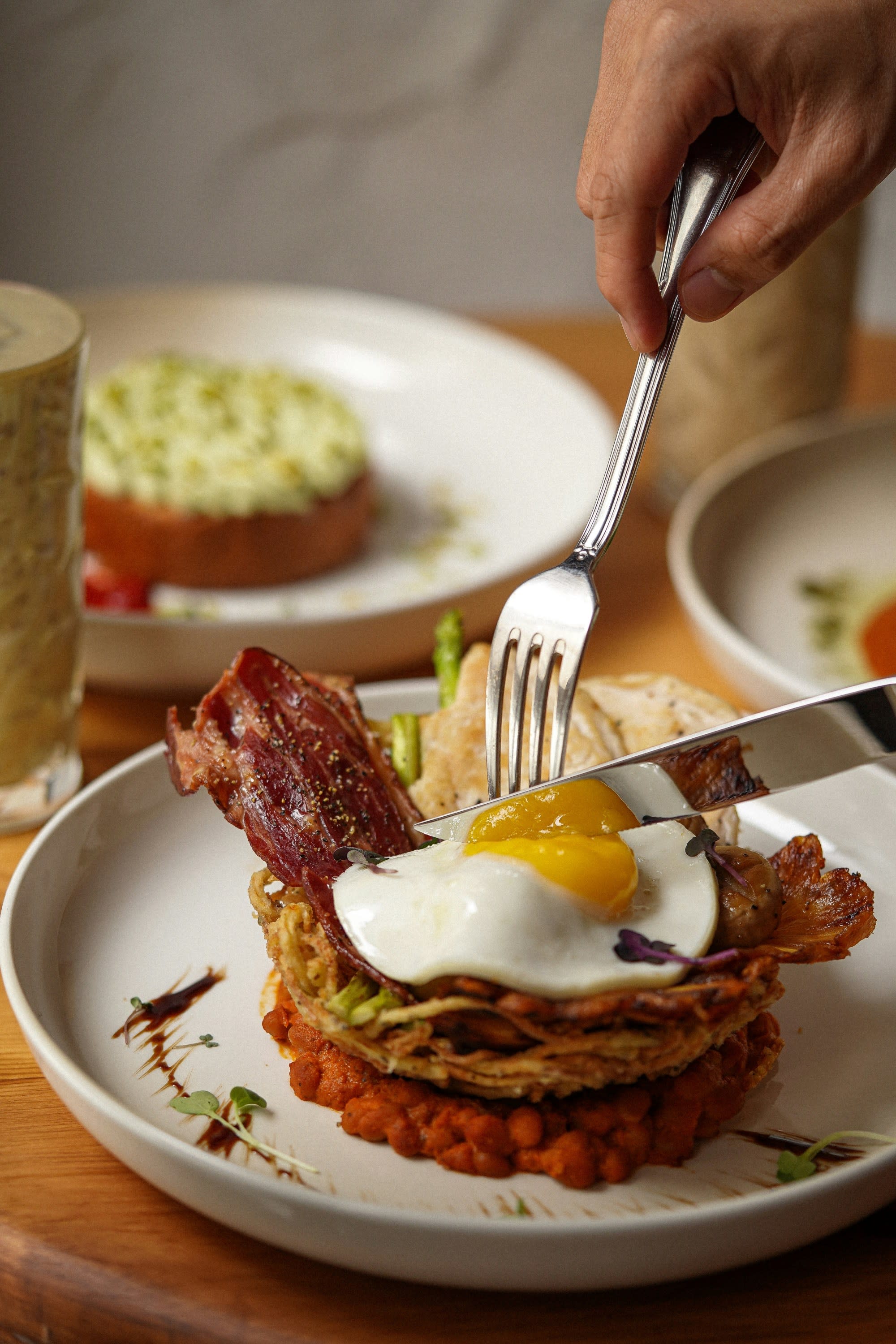 A person using a fork and knife to cut into meat topped with a fried egg, like you might get at one of the best restaurants Glasgow.