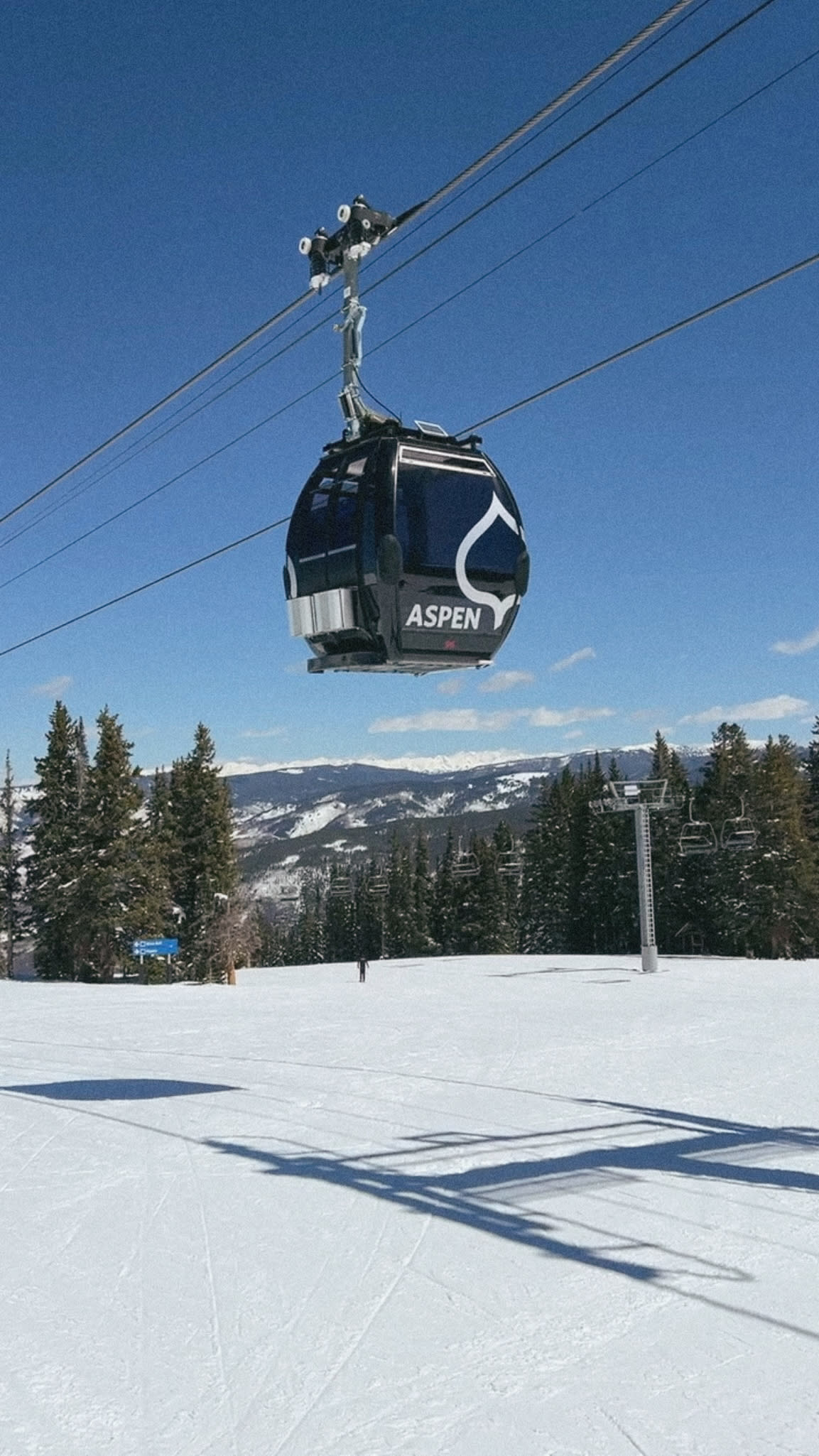 A gondola style ski lift above the snow, mountains, and frosted trees in Aspen during winter.