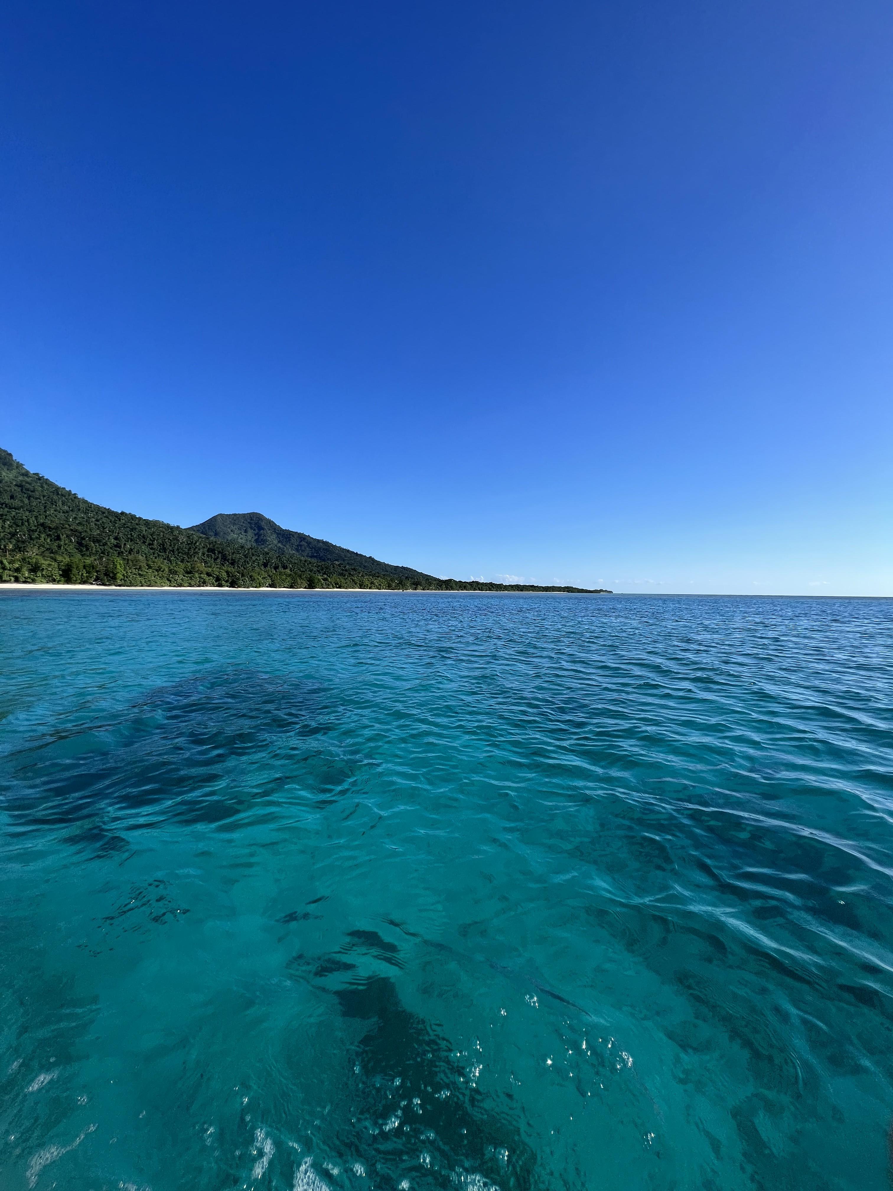 Clear blue waters and a small hill on a beach seen from a boat.