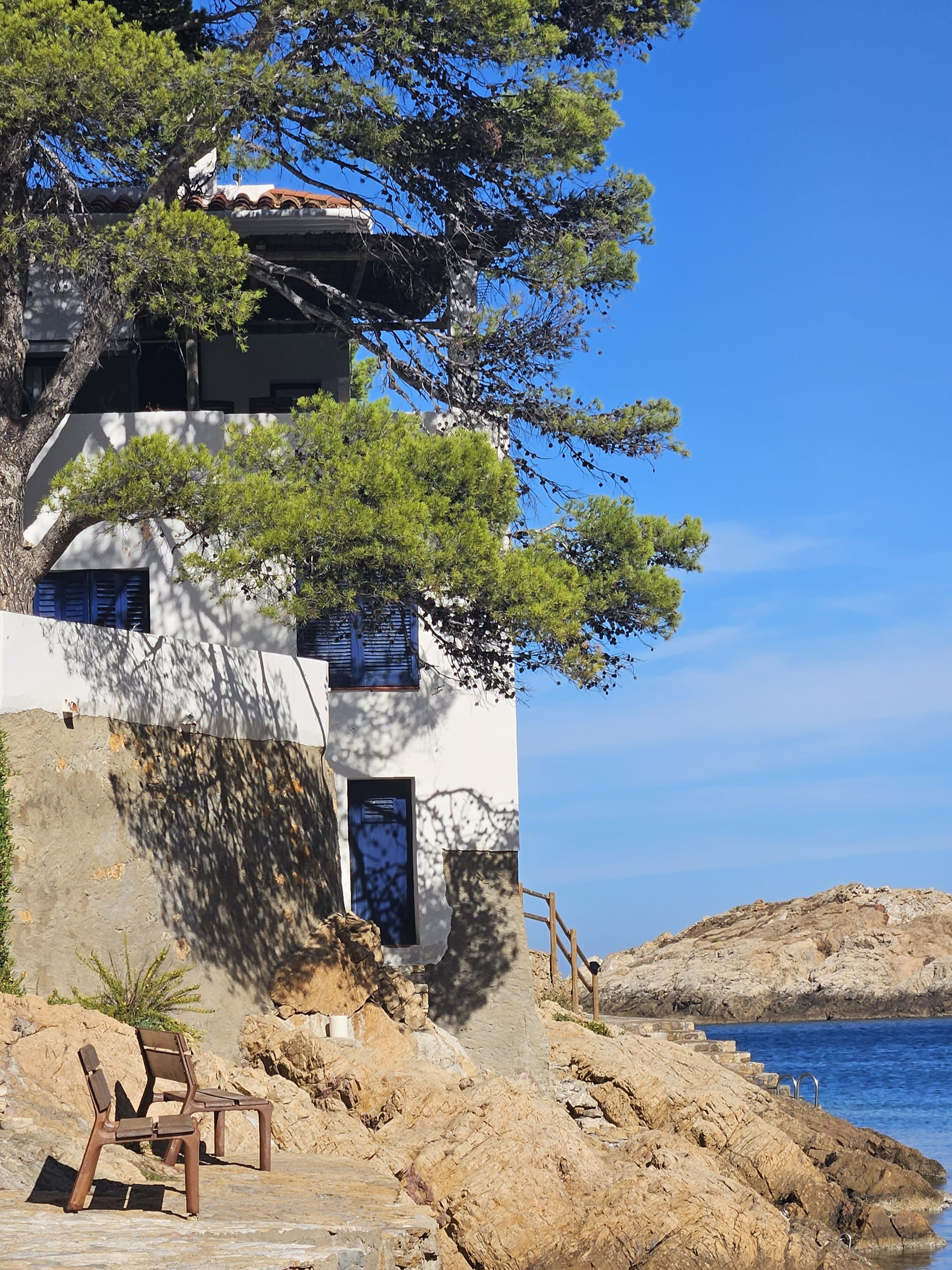 A white and blue house built into the rocky terrain on the coast of Begur, on a sunny day in Spain.