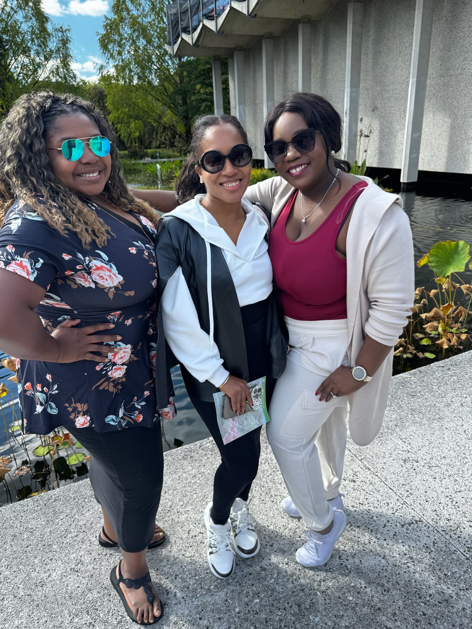 Tysheda and two friends standing on a sidewalk outside of a concrete building surrounded by greenery.