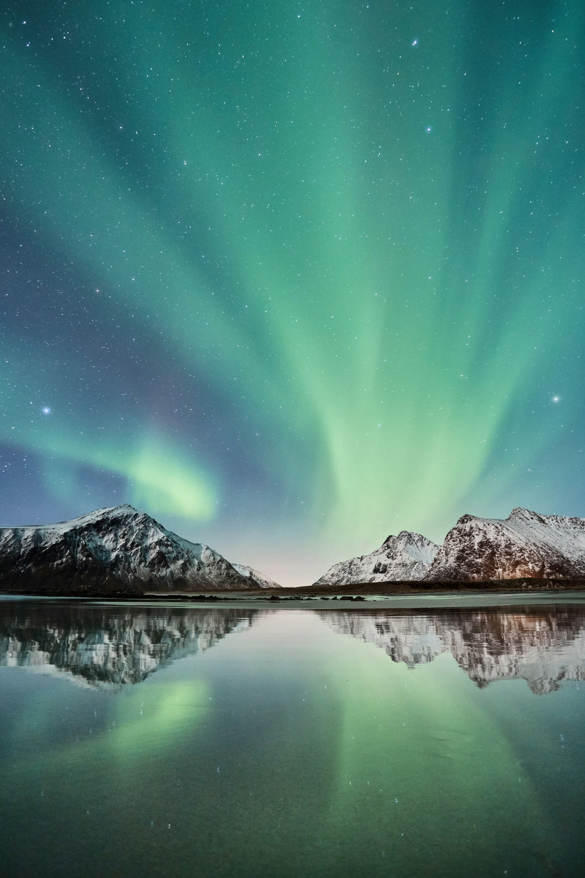 Green and blue natural lights in the sky over mountains and a body of water