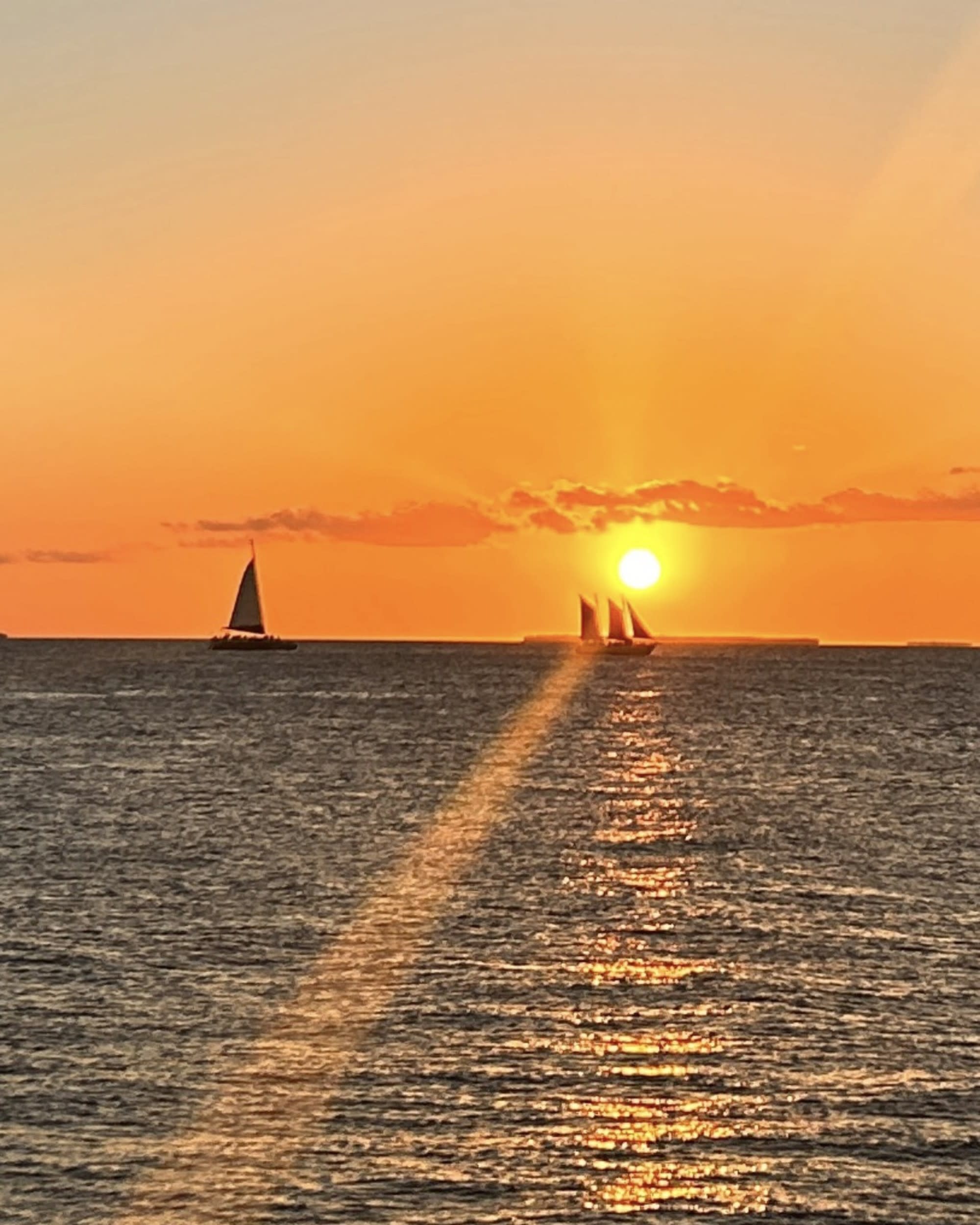 The image portrays a serene sunset over the ocean, with sailboat silhouettes against a vibrant orange sky.