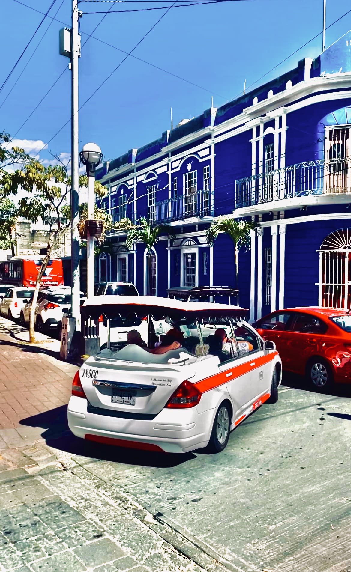 An air taxi and other cars in front of a blue building on a sunny day.