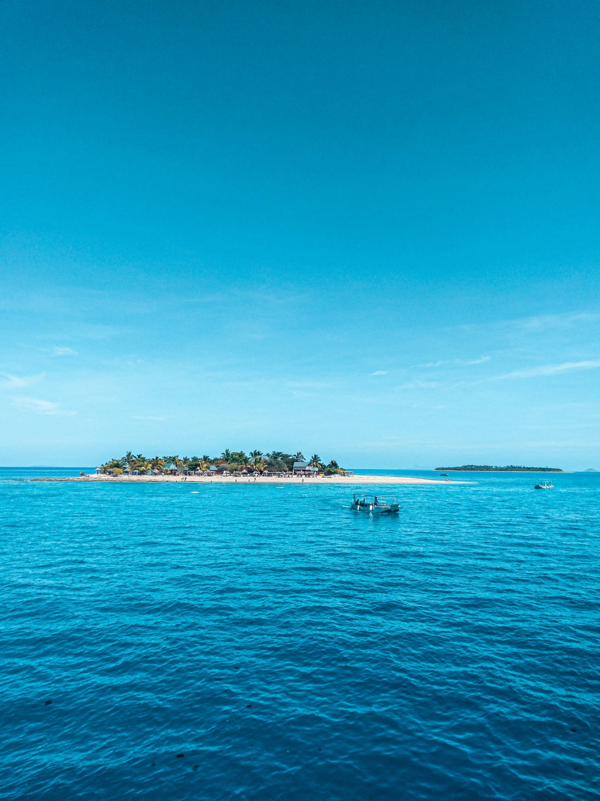 A tranquil tropical seascape with a boat on the water and an island in the distance, under a clear blue sky.