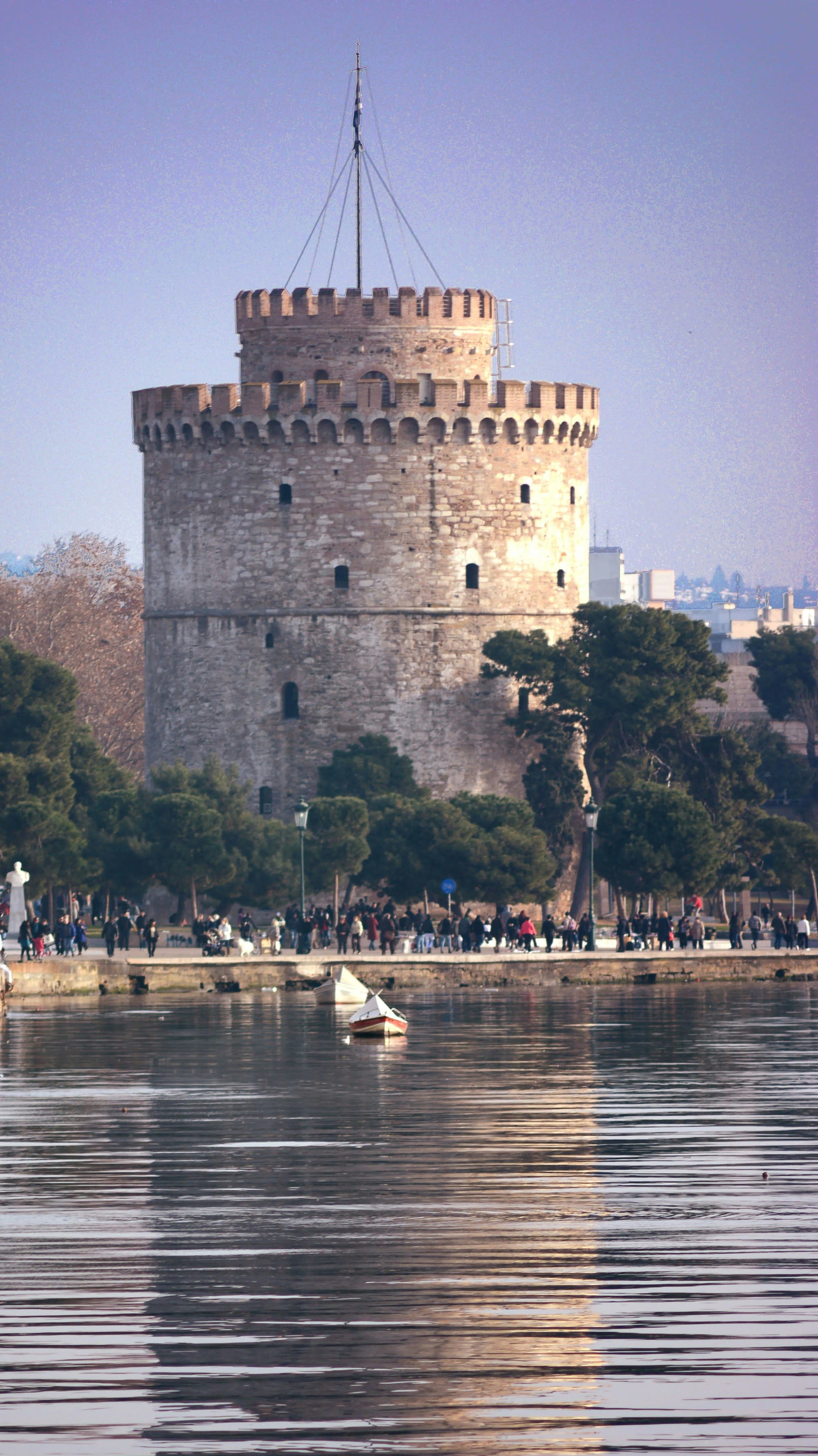 A majestic stone tower in a city in Croatia beside tranquil waters, with a small boat and visitors enjoying the serene setting.