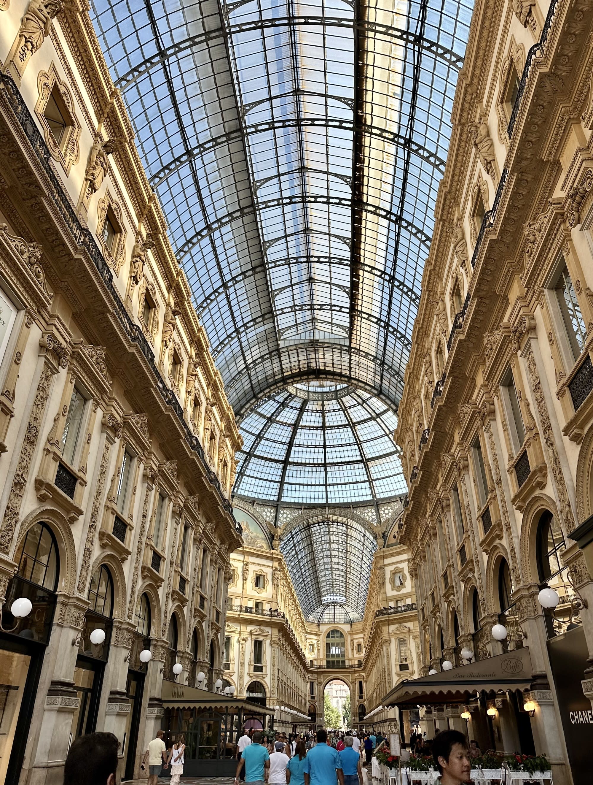 The image features an ornate gallery with a glass dome ceiling, bustling with visitors and lined with shops.