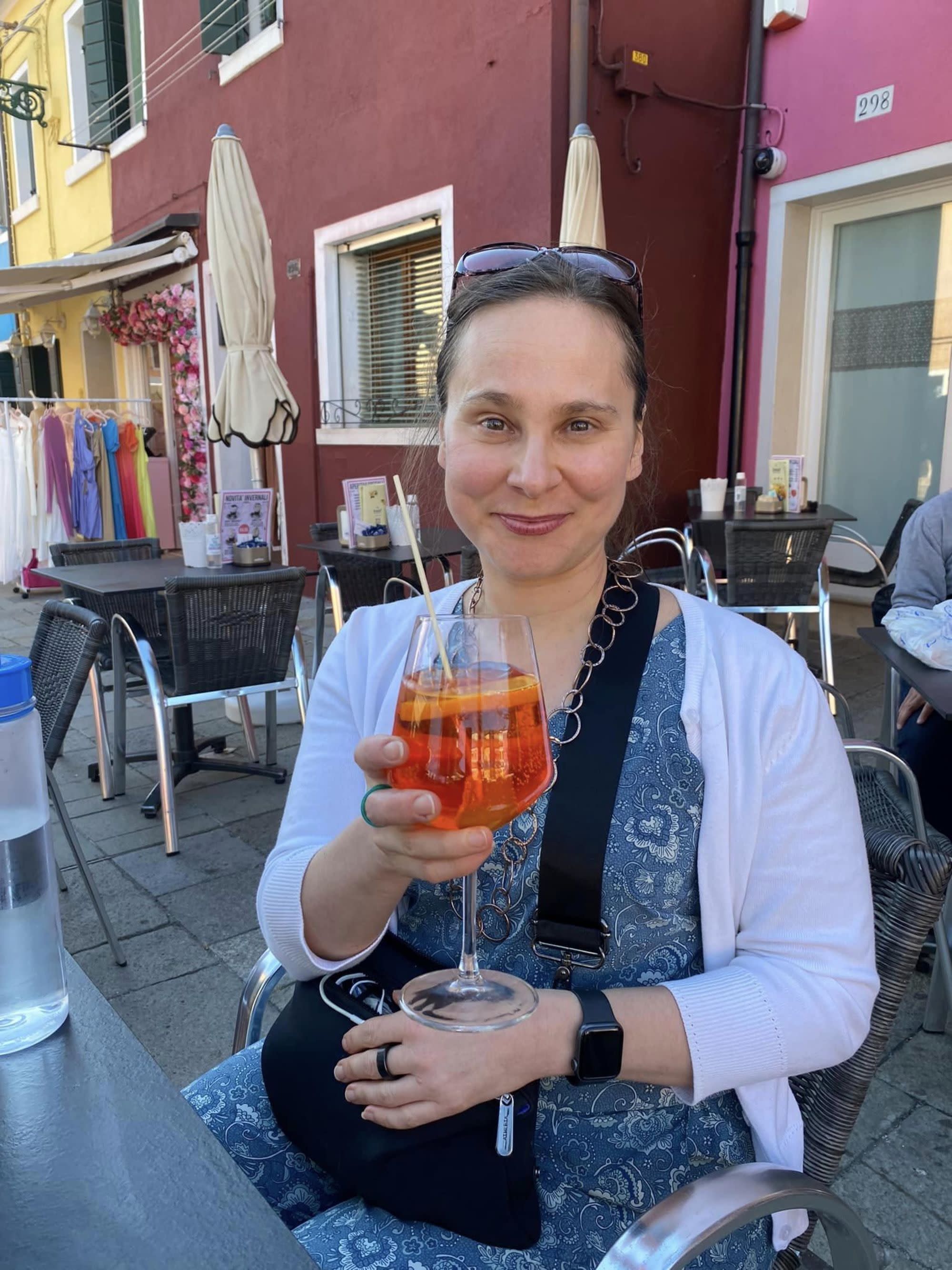 A person enjoys a refreshing orange drink at an outdoor café, with vibrant buildings and a lively atmosphere in the background.