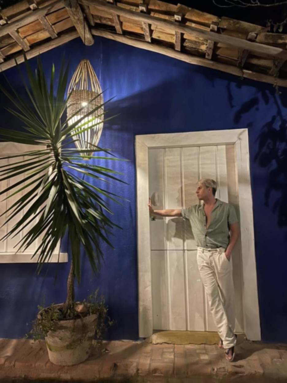 A man earing a green shirt and white pants posing in front of a white doorway and blue wall