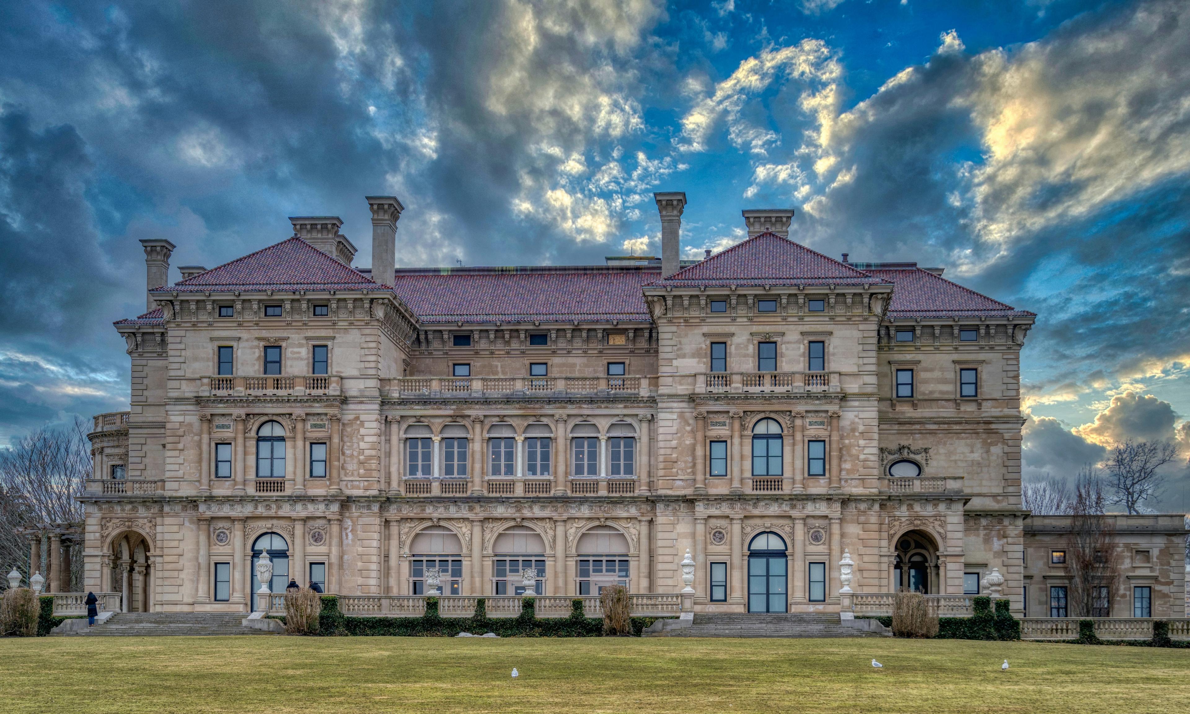A mansion in Newport, Rhode Island, with a lush lawn in front, and a semi-cloudy sky.