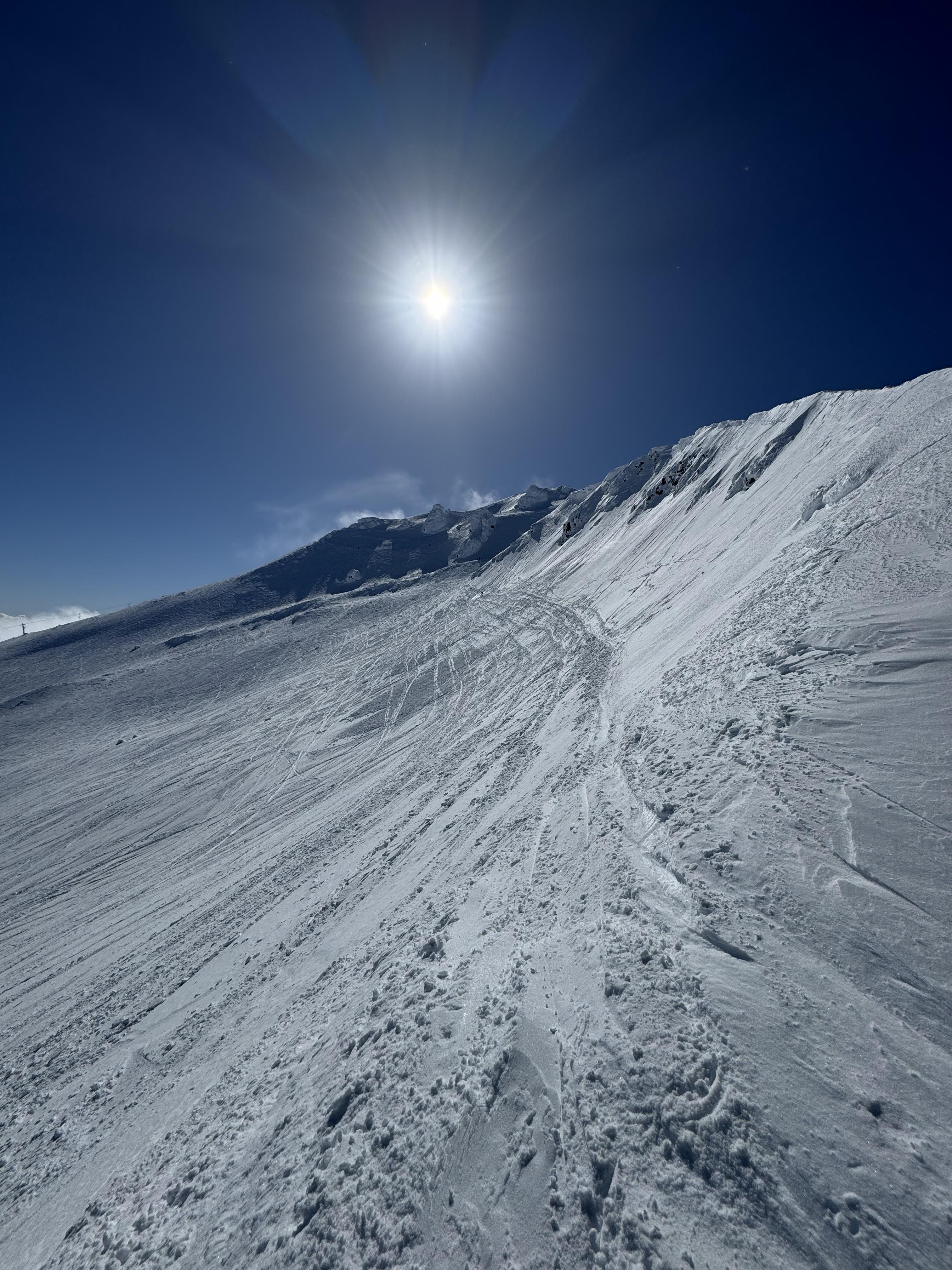 The sun shining over a slanted snowy hill.