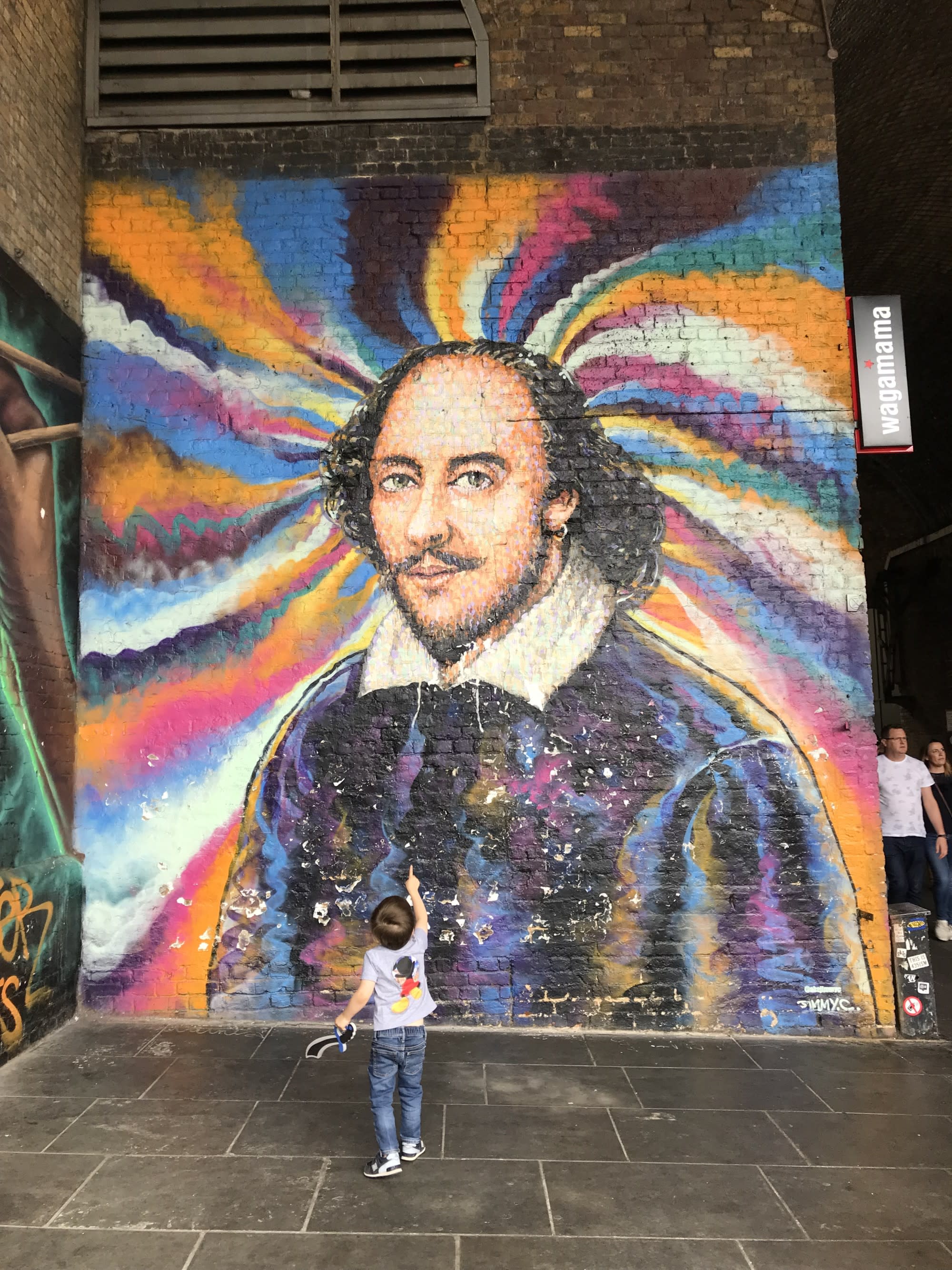 Kid looking and pointing at colorful wall art of a man.