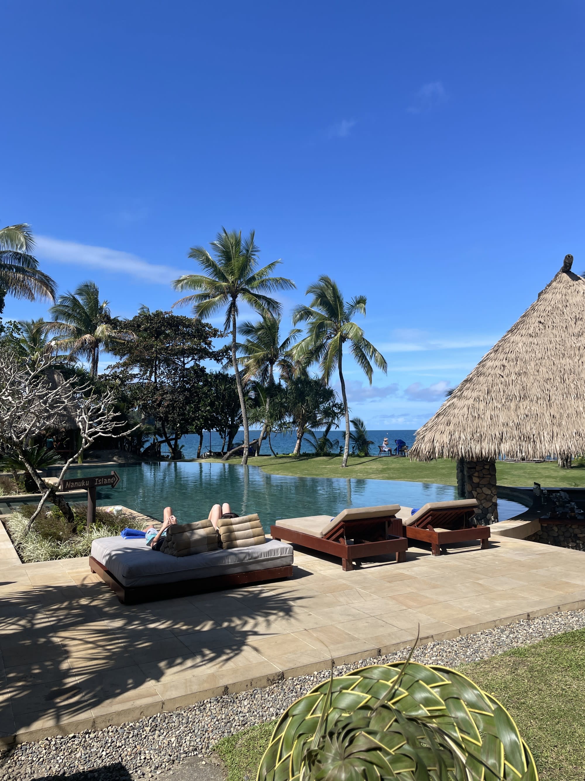 Lounge chairs near a pool next to a hut during daytime.