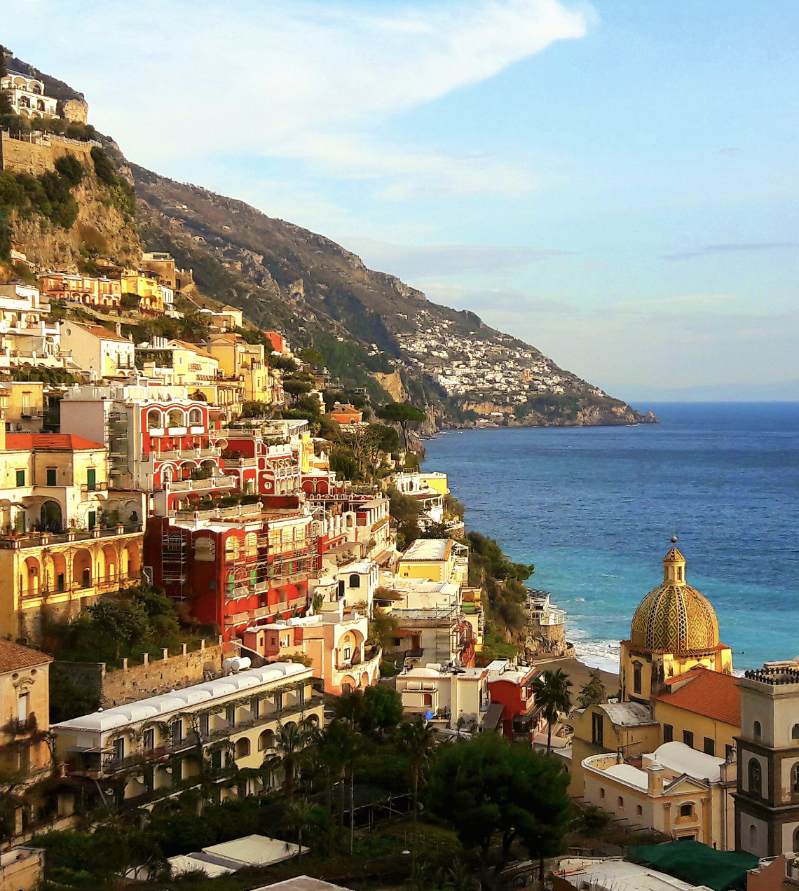 A picture of the vibrantly colorful town of Positano, with various buildings nestled into a mountain. There is also a view of the blue sea in the background towards the right of the image.