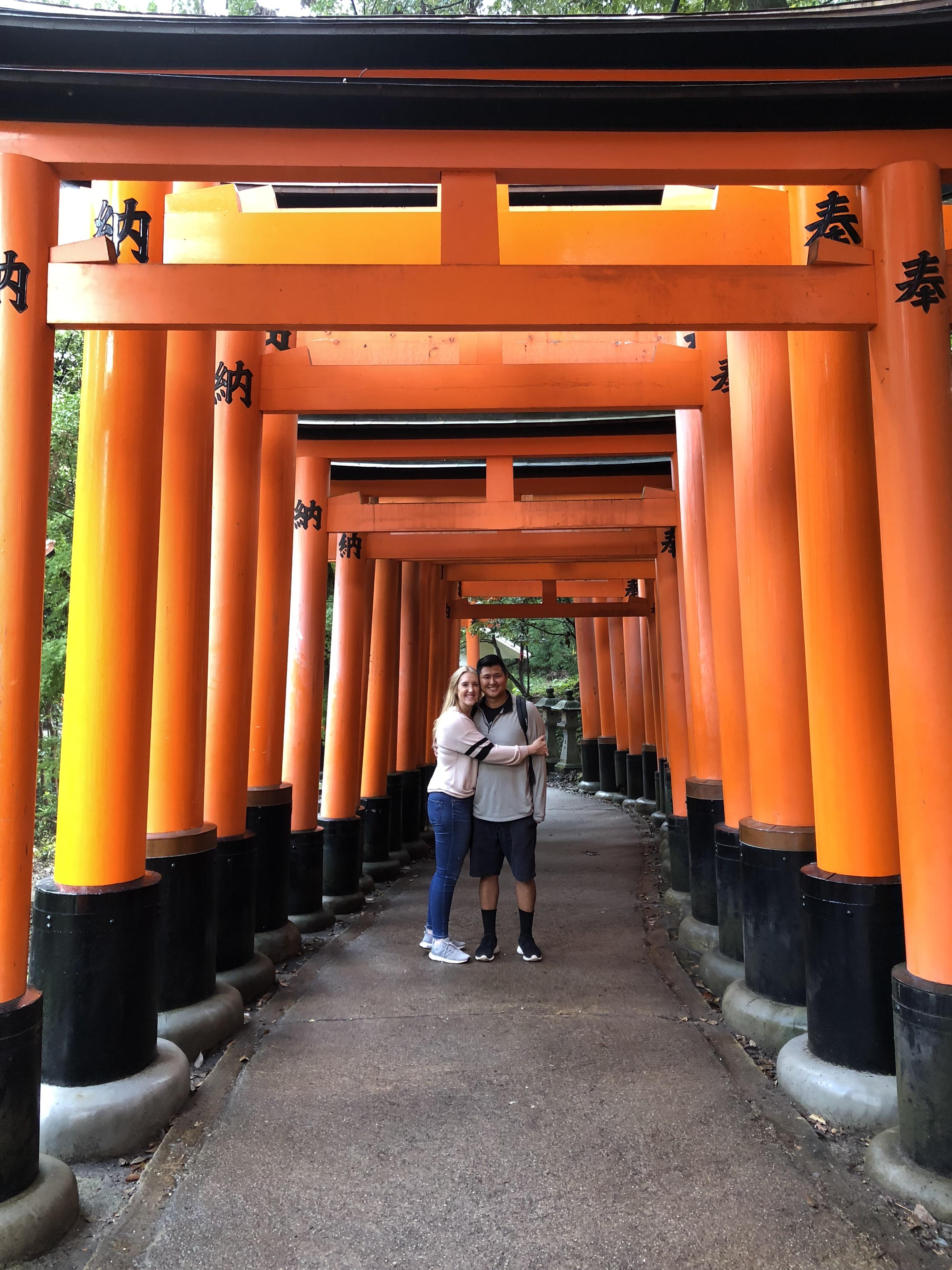 Two people posing beneath the red arches of the Fushimi Inari Shrine.