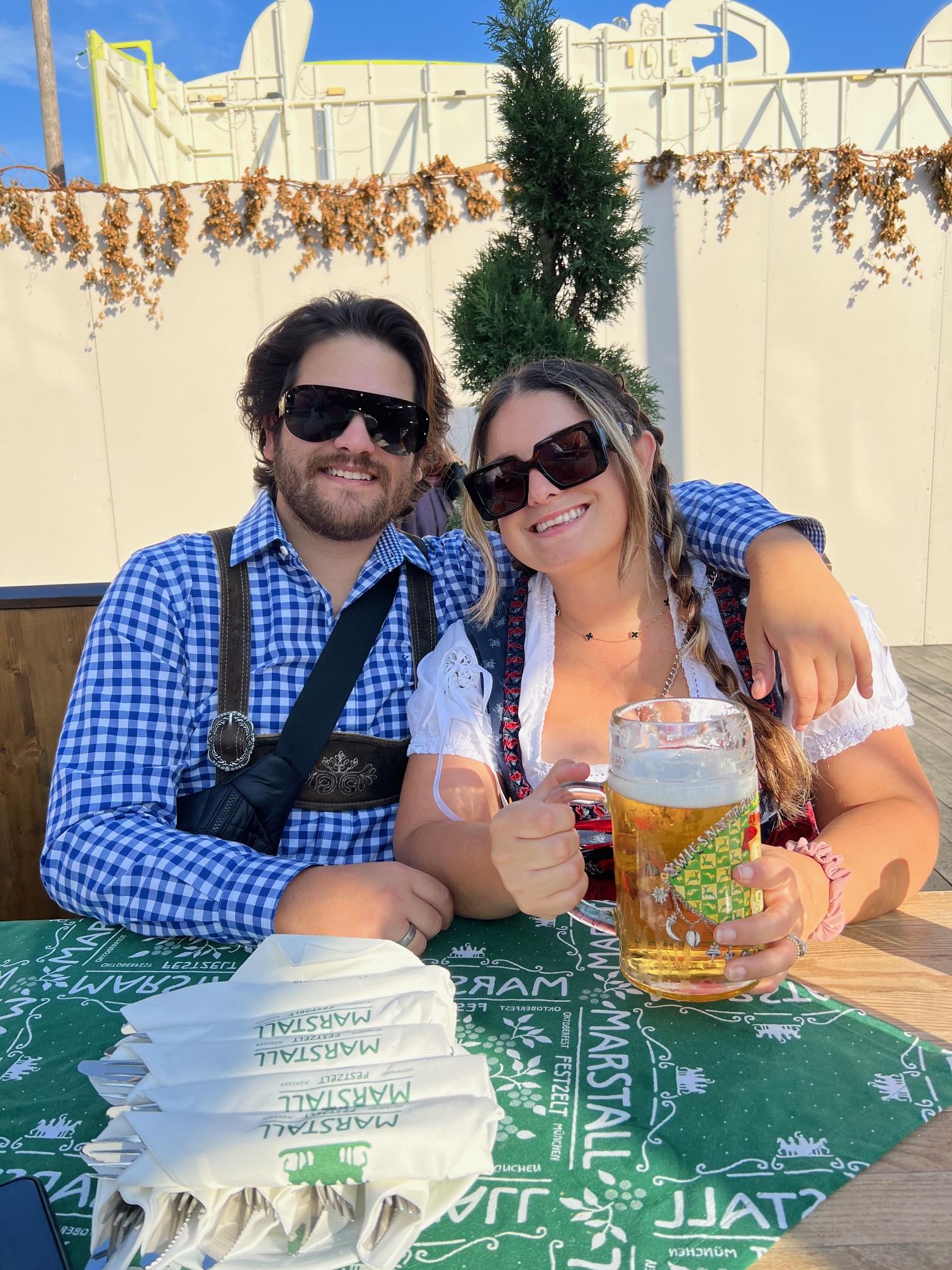Couple posing in traditional Oktoberfest outfits with beers.