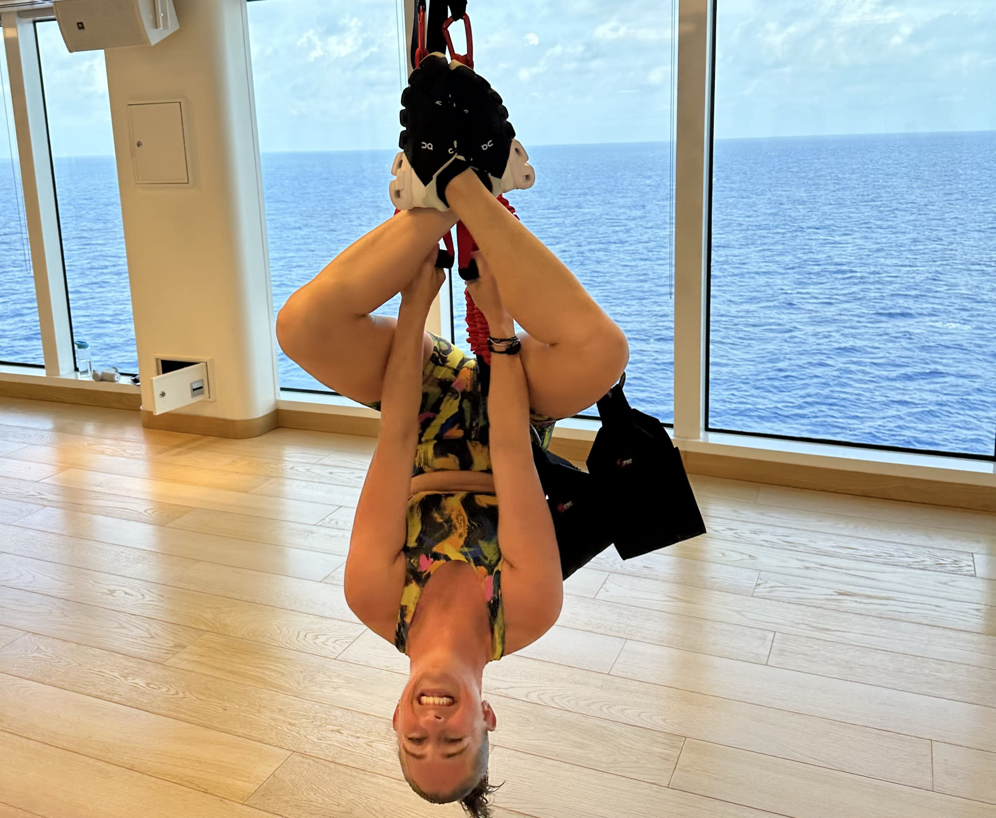 A girl hanging upside down by a rope with blue water in the background.
