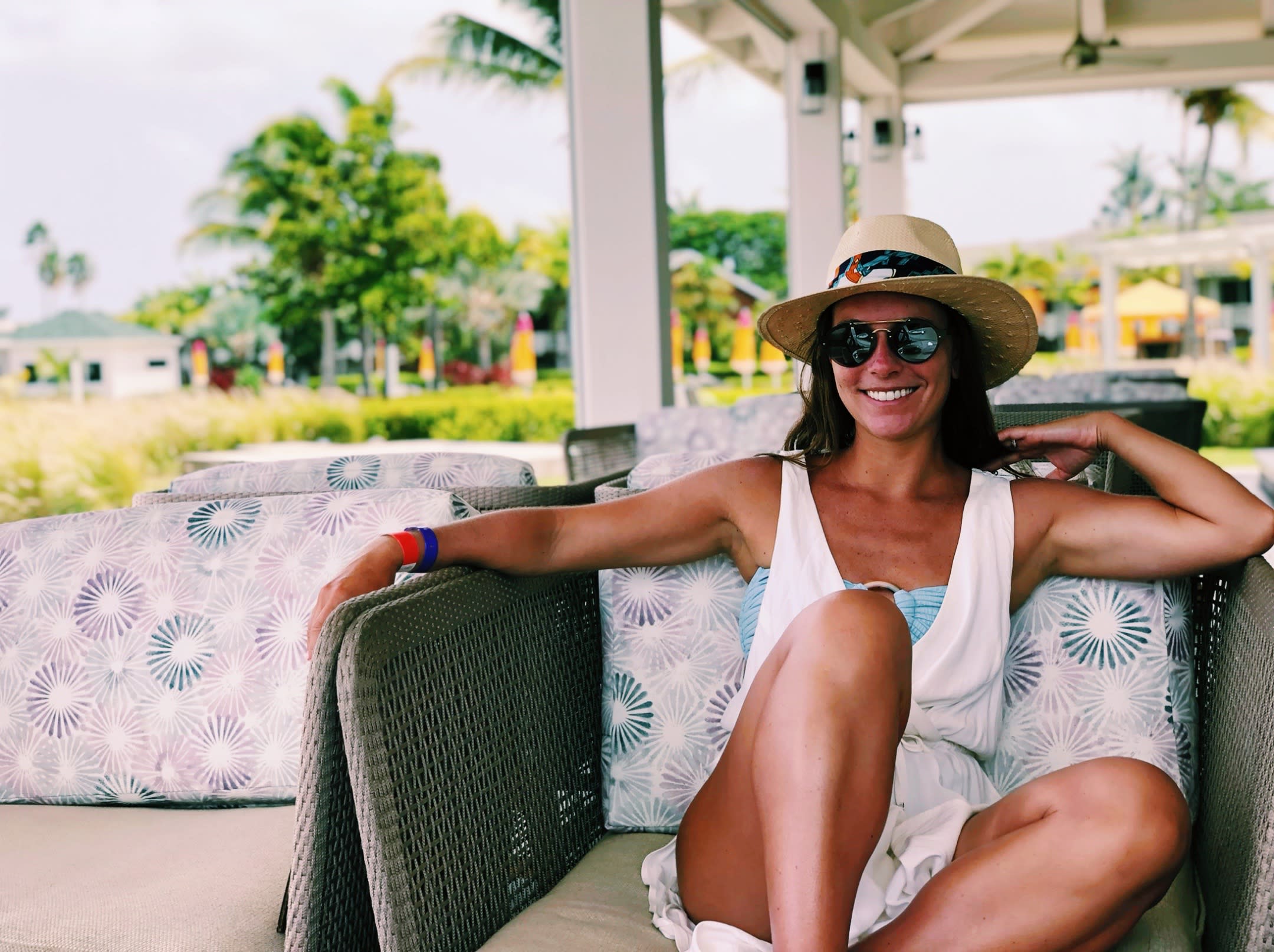 a woman in a hat and sunglasses sits on a chair in a tropical destination